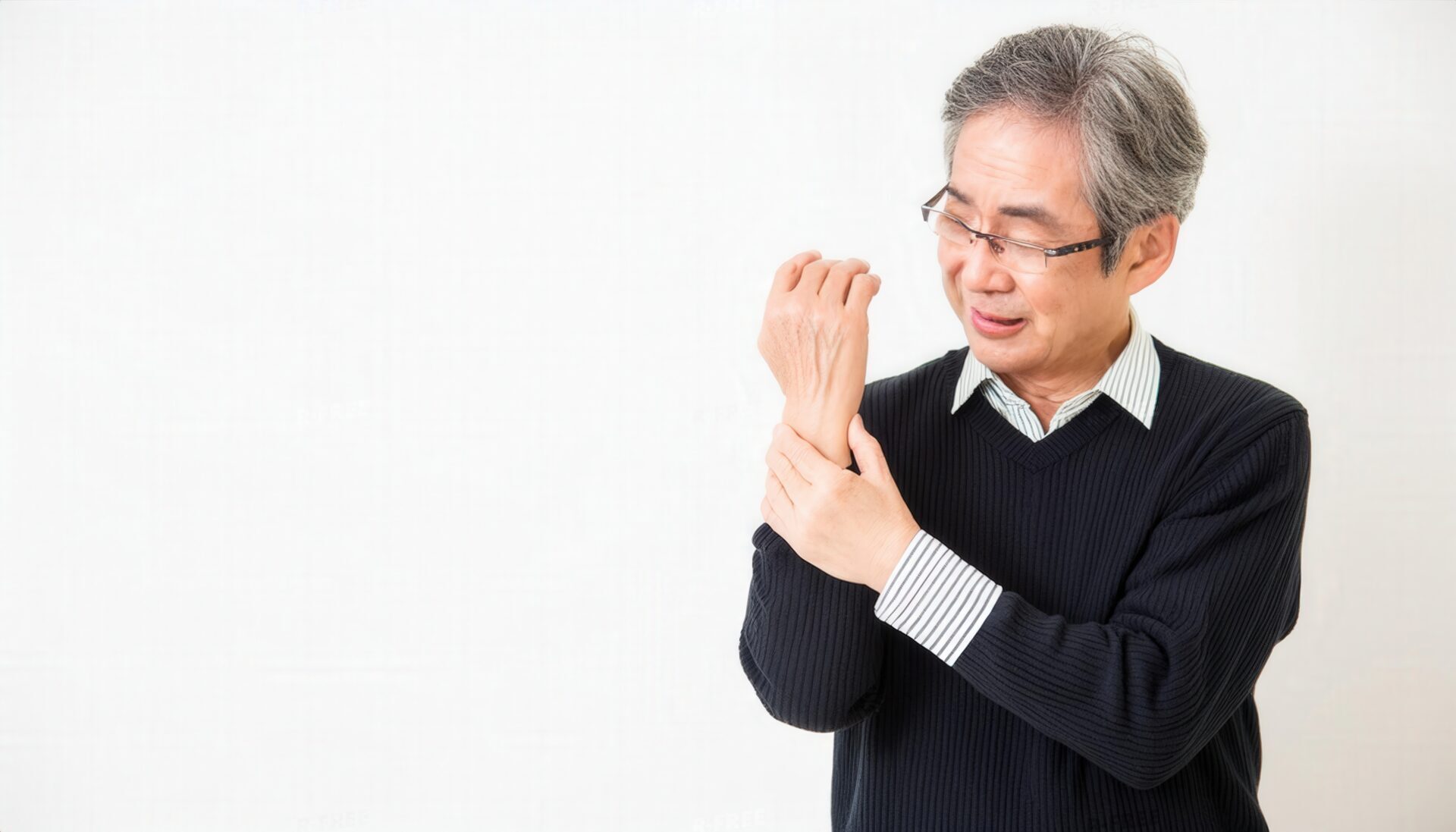 眼鏡をかけ右手首を押さえる白髪混じりの男性