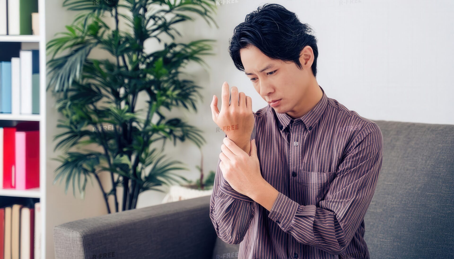 本棚と植物を背景に右手首を押さえる男性