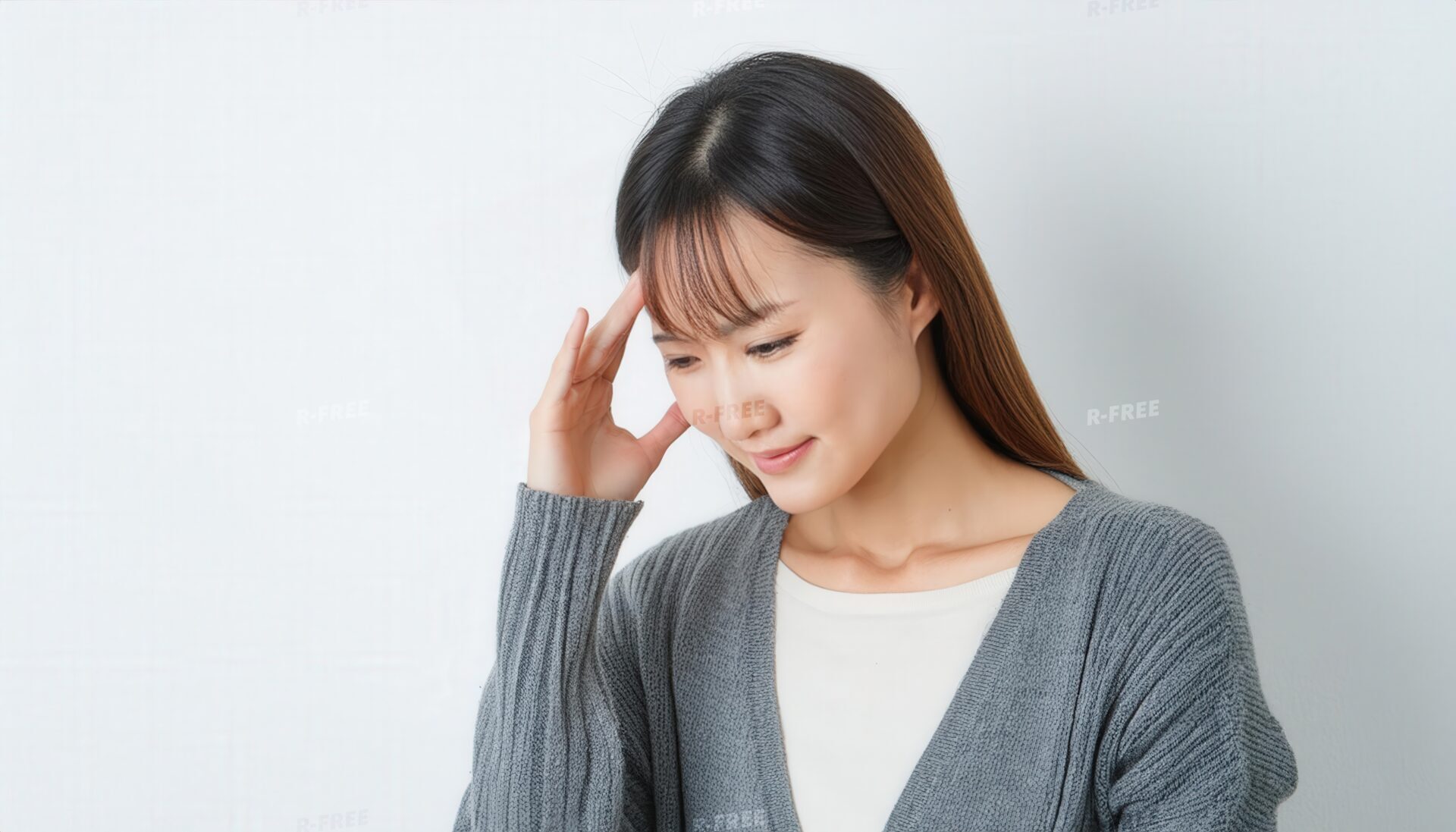 頭痛を感じる女性のこめかみを押さえる伏せ目の姿