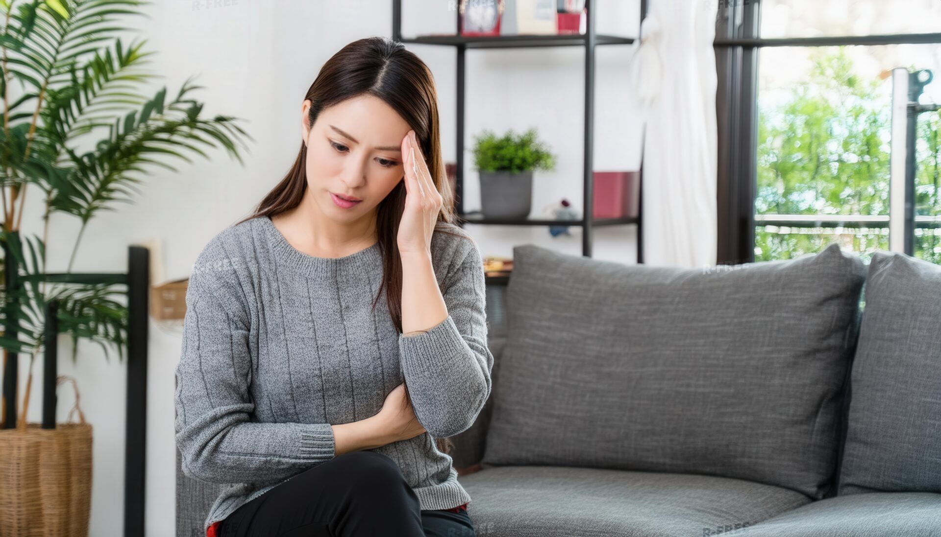 頭痛を感じる女性のソファで額を押さえる辛そうな表情