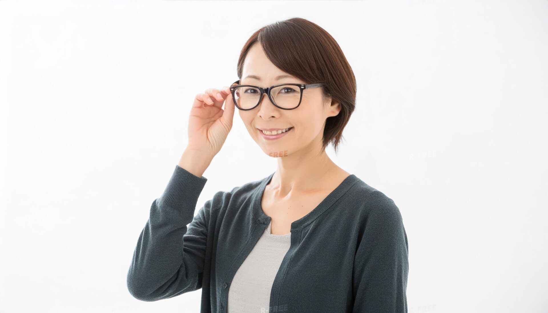 黒縁眼鏡に右手を添えて微笑む濃灰色カーディガンの笑顔の女性