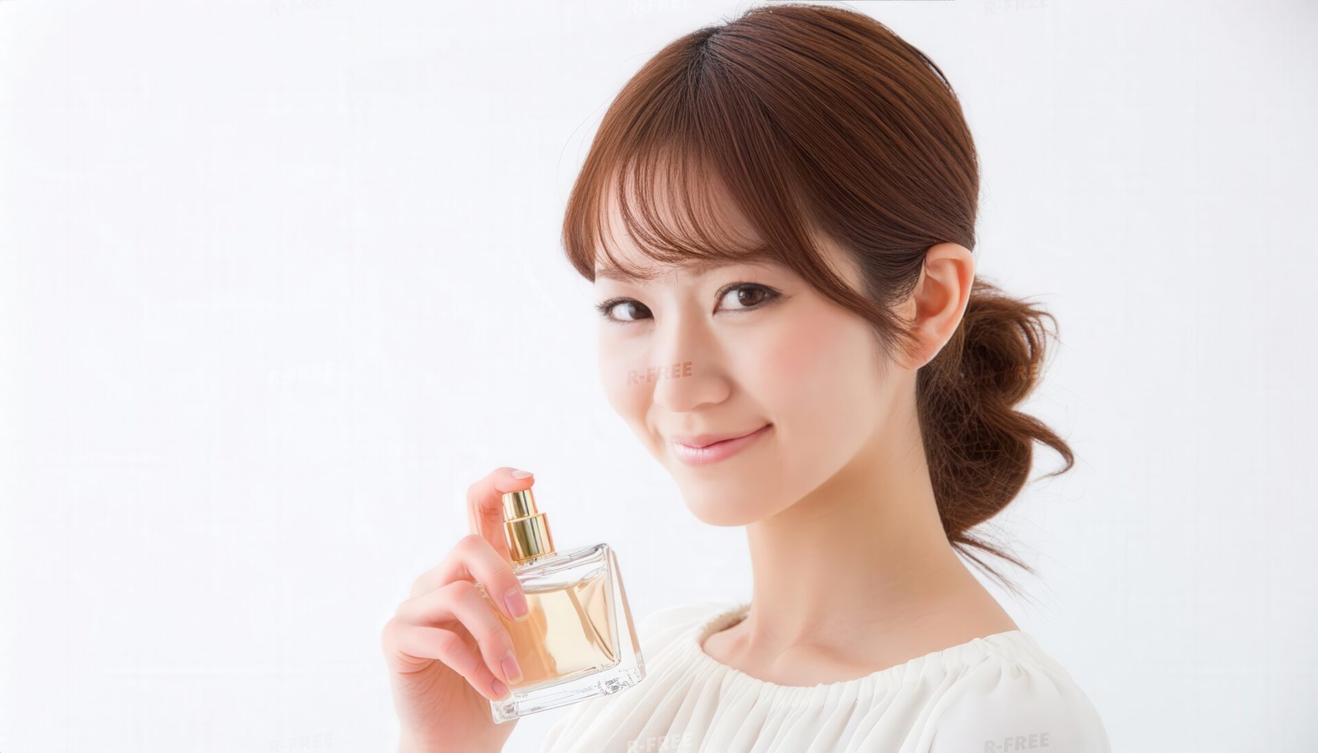 お団子ヘアの女性が琥珀色の香水を手に微笑む