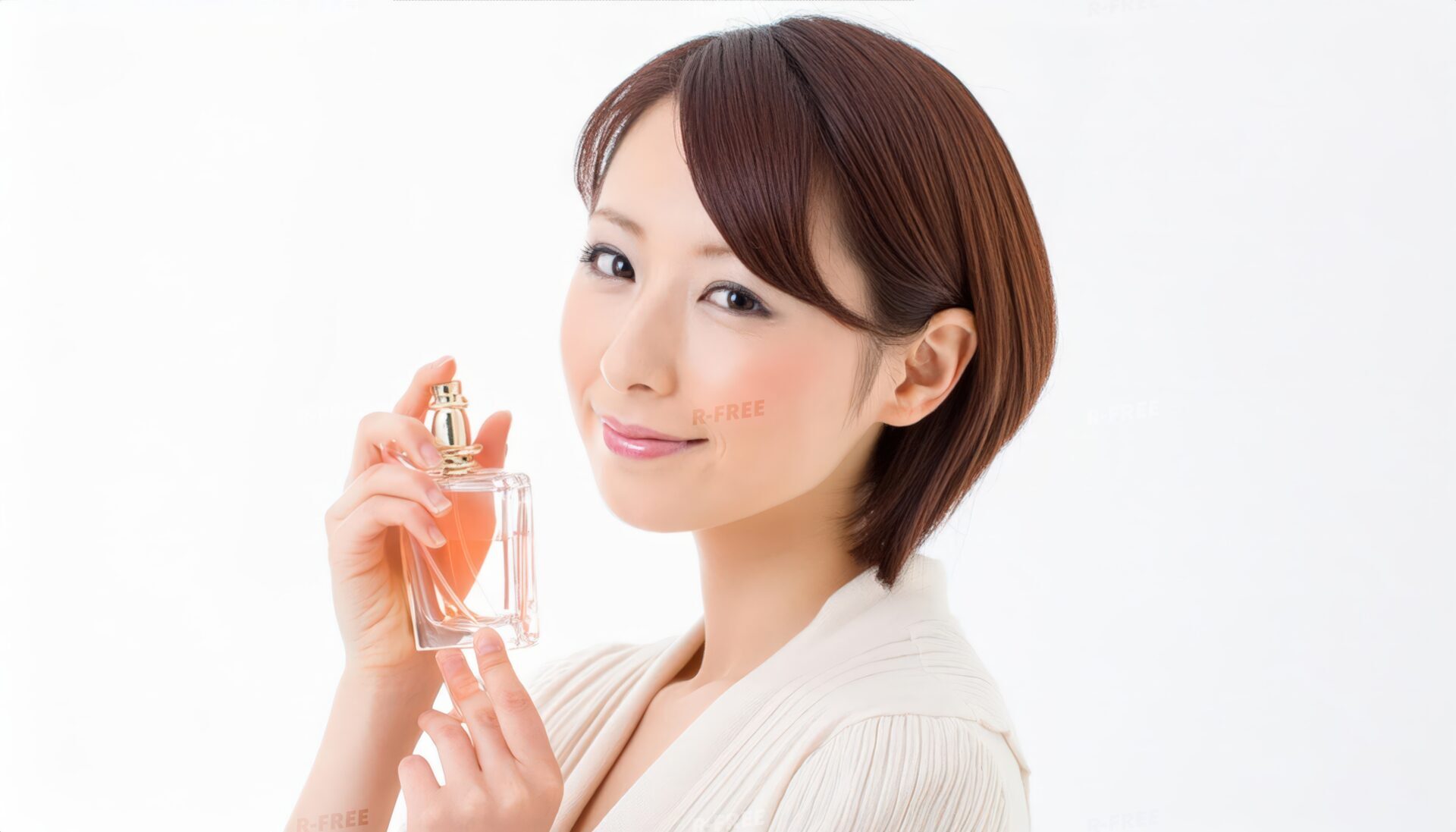 短い茶髪の女性が香水を手に穏やかに微笑む