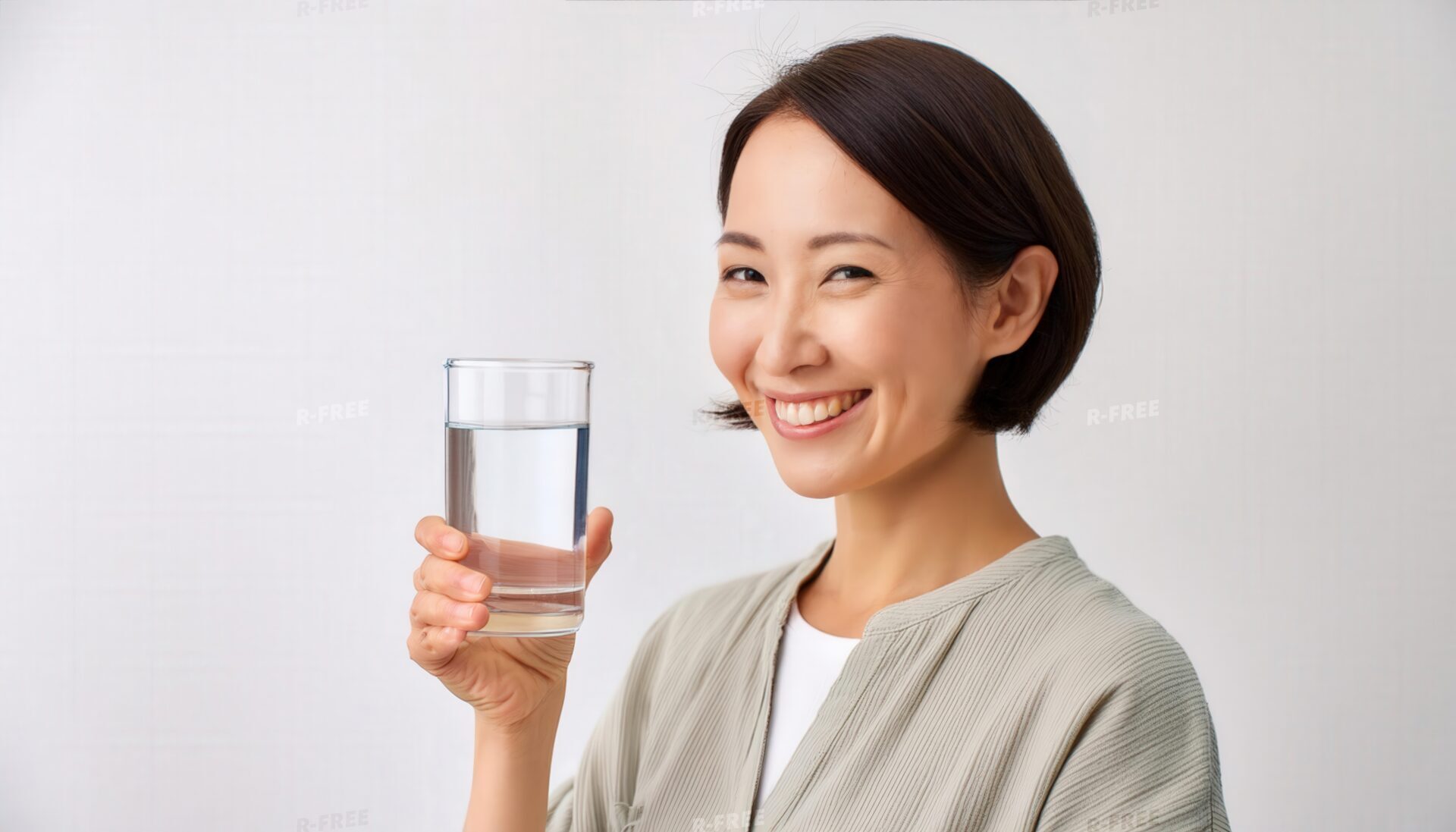 笑顔で正面を向きグラスの水を手に持つ30代女性