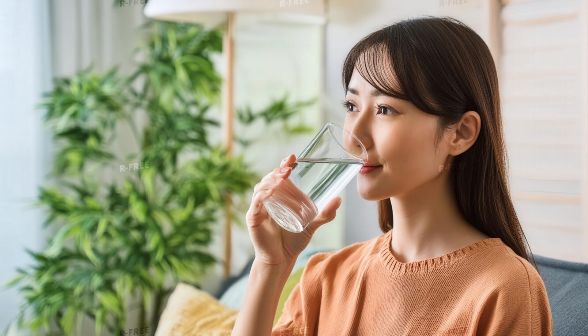 穏やかな表情で水を飲むオレンジ色トップスの女性