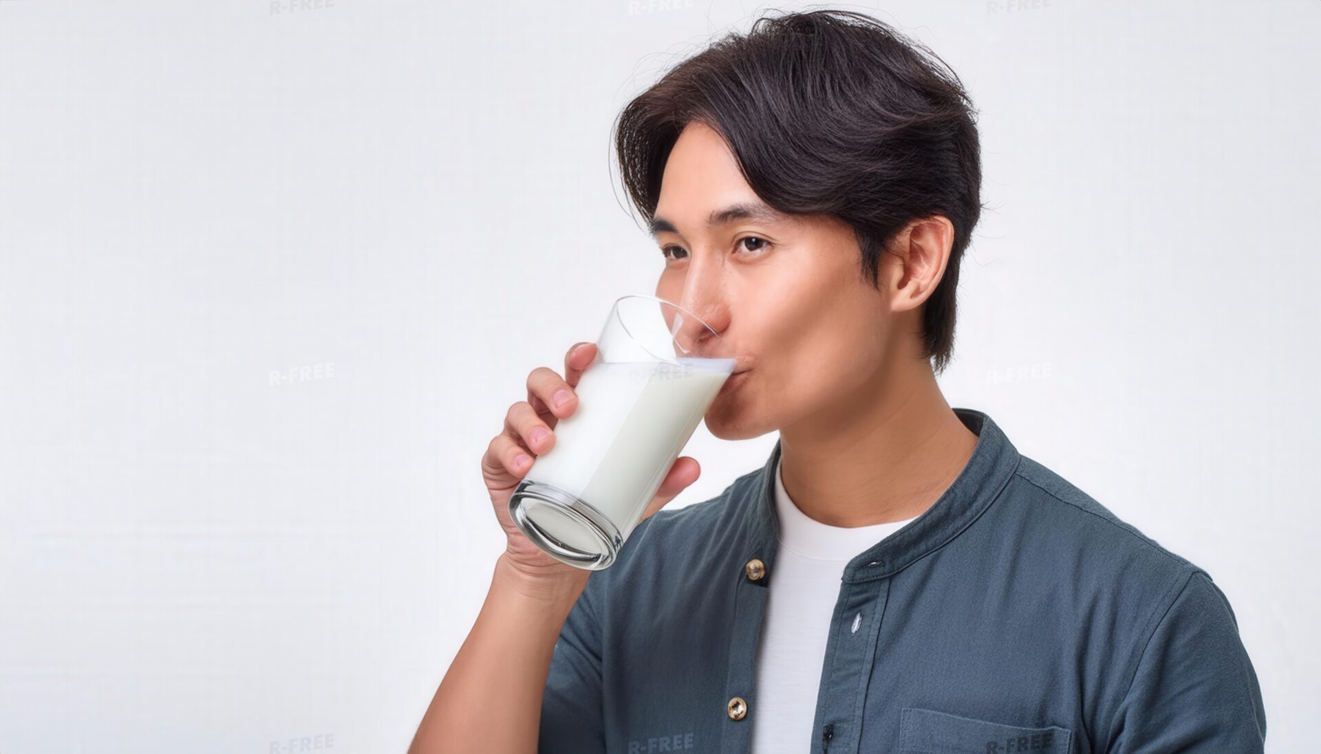 白Tシャツと青灰色シャツ姿で横向きに牛乳を飲む男性