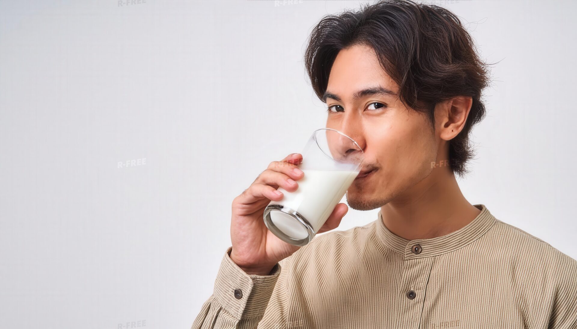 ベージュのシャツ姿でカメラを見ながら牛乳を飲む男性