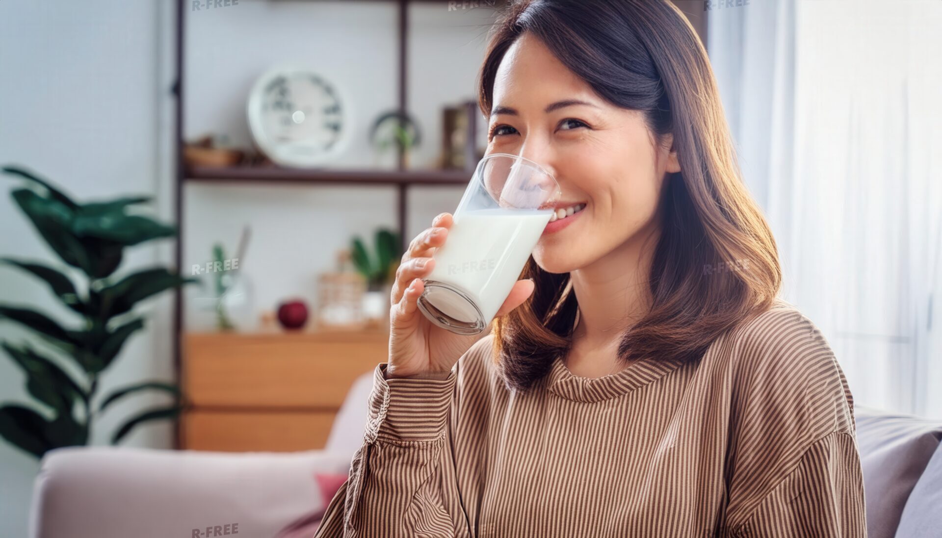 室内で牛乳を飲む若い女性（ブラウンのトップス）