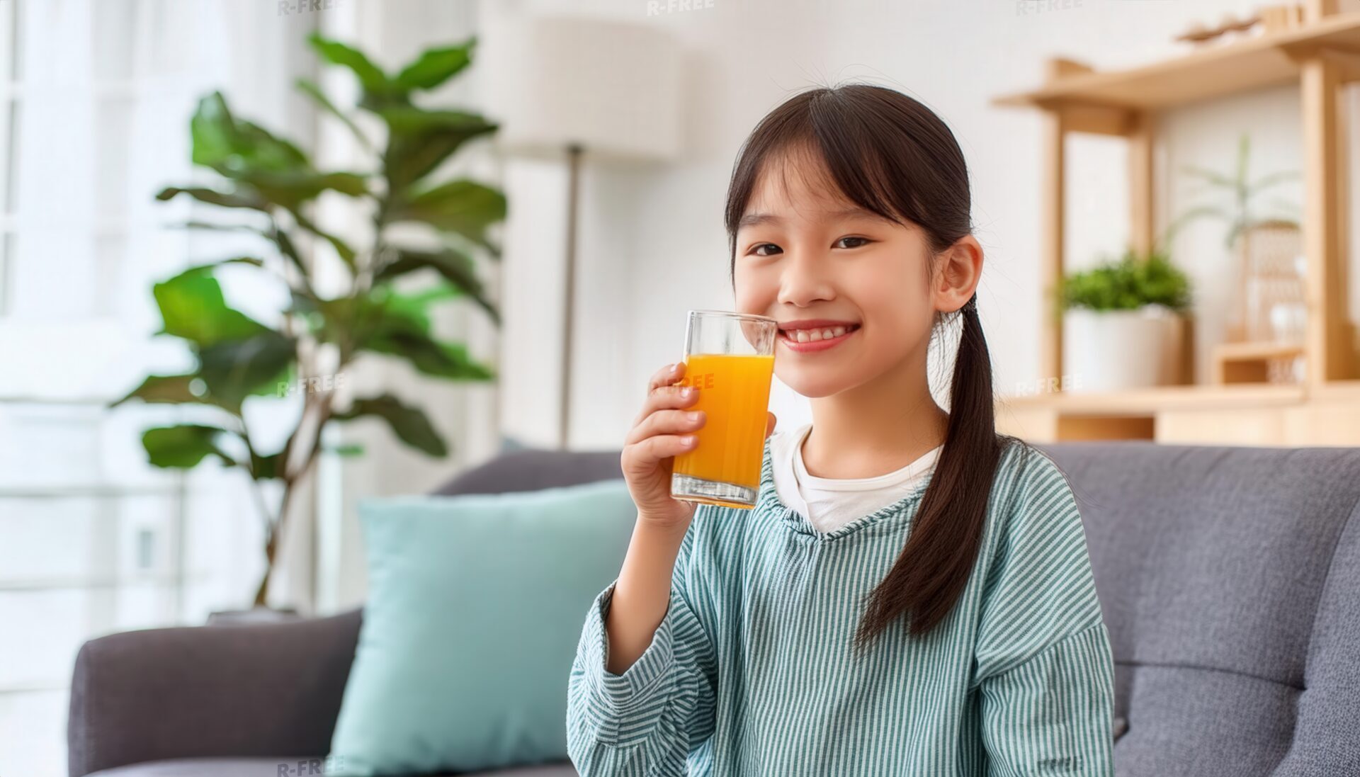 リビングでストライプ服の女の子が笑顔でオレンジジュースを飲む子供