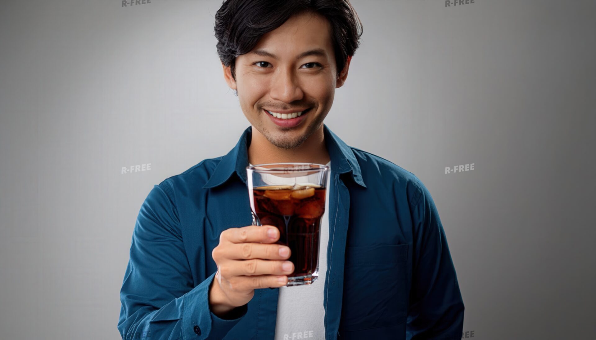 グレー背景で黒い炭酸飲料のグラスを差し出す若い男性