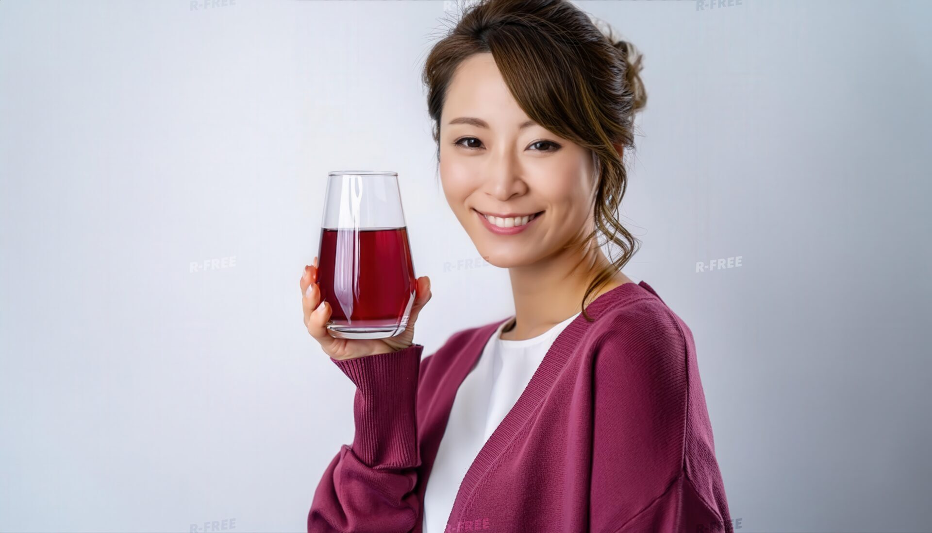 グレー背景で赤紫色のグレープジュースを持つ若い女性