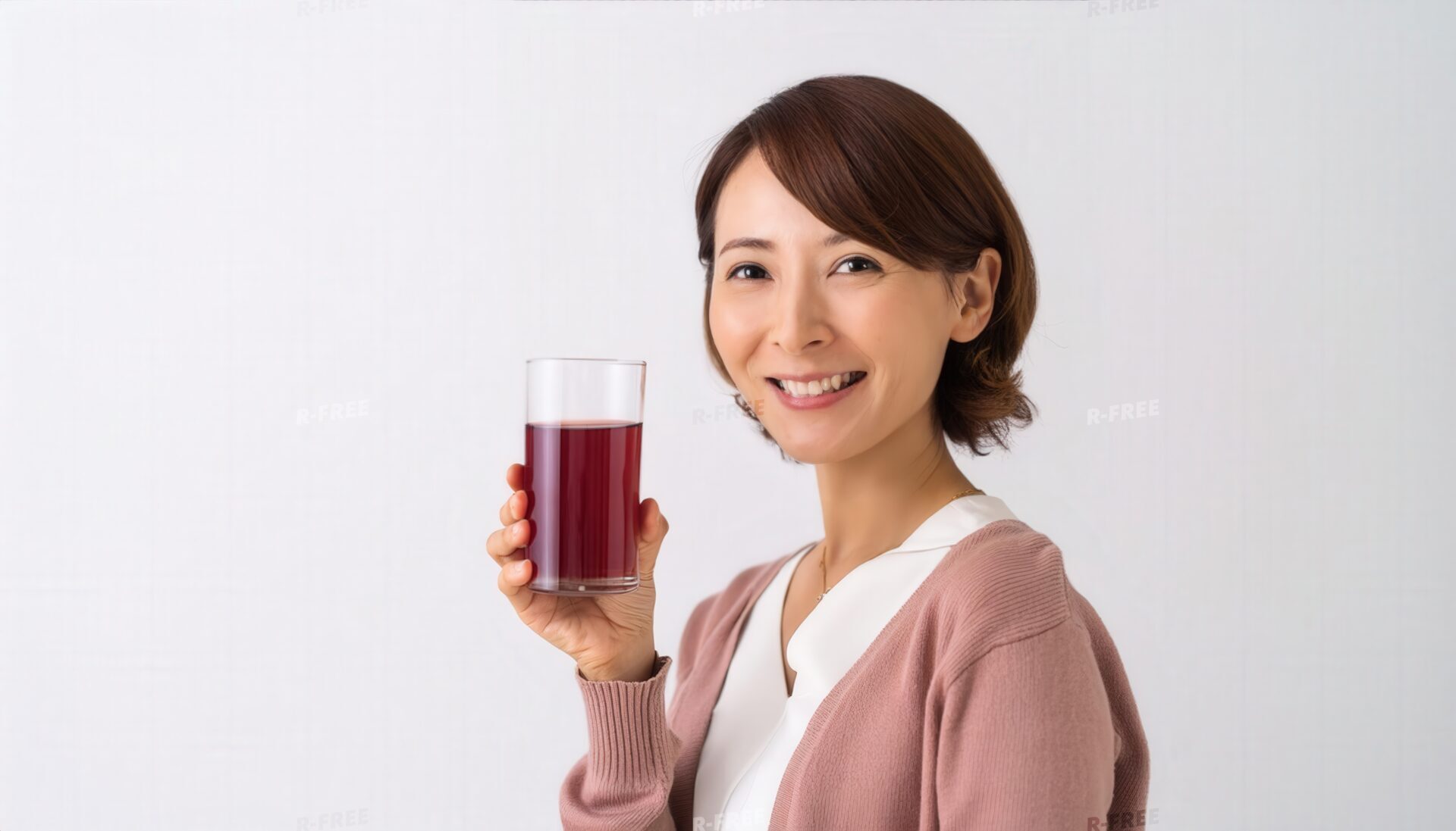 白トップスと淡いピンクカーディガンで笑う30代女性