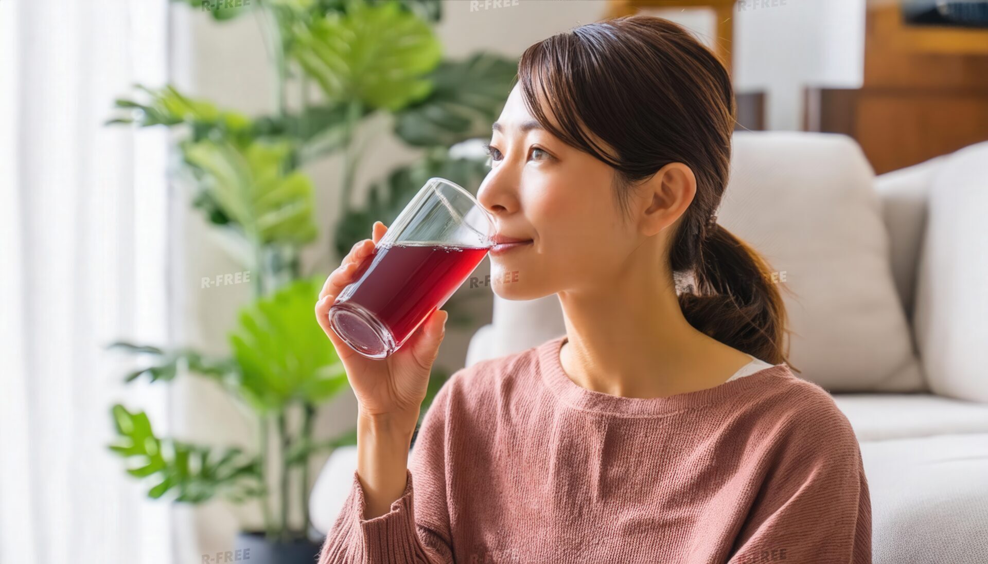 リビングで髪を束ねてグレープジュースを飲む20代女性
