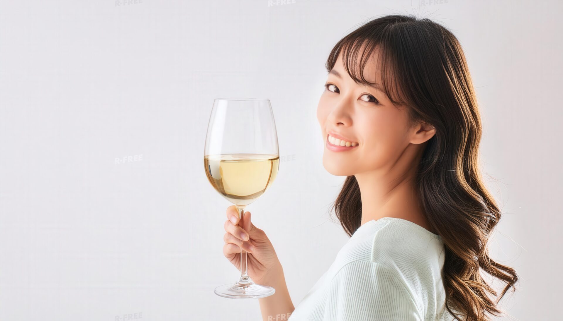 白背景で白ワインを持ち笑顔で振り返る20代女性