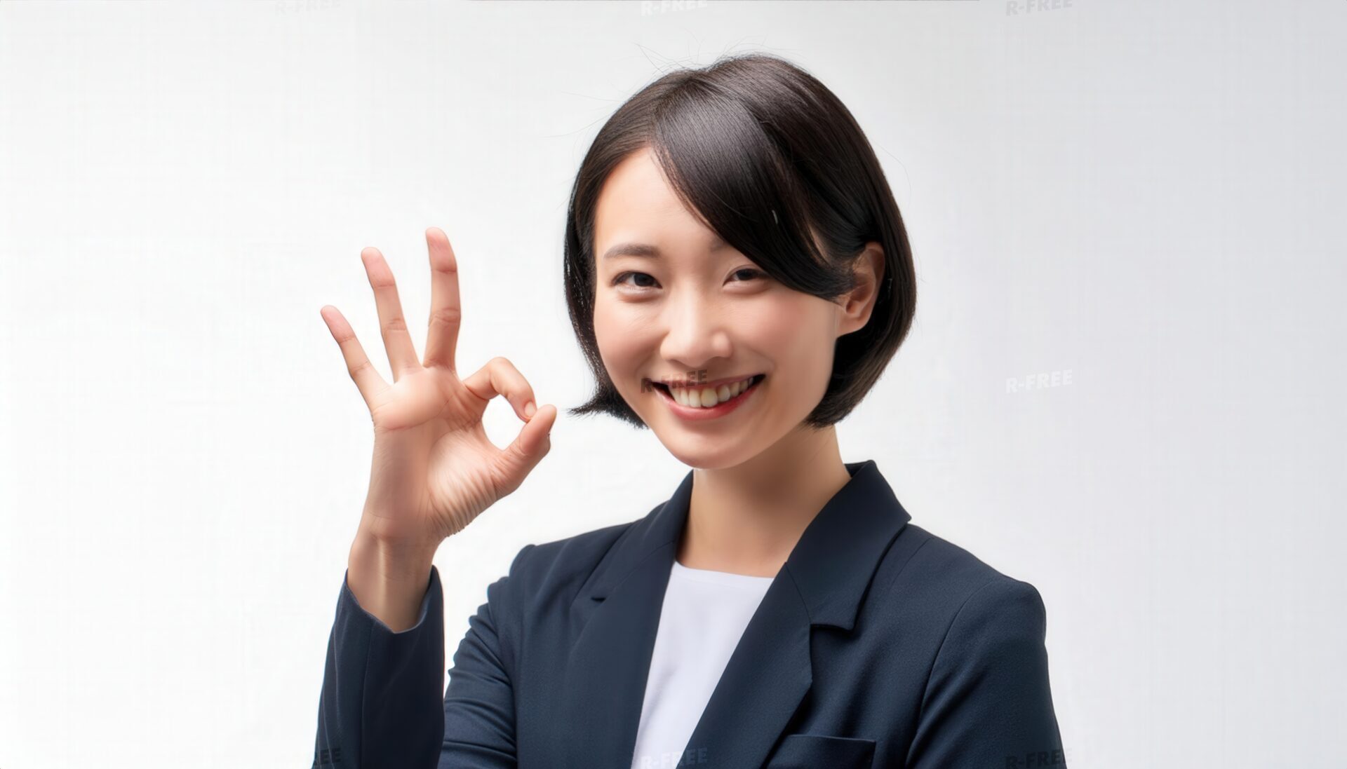 白背景で紺色ジャケットを着た女性のOKサイン
