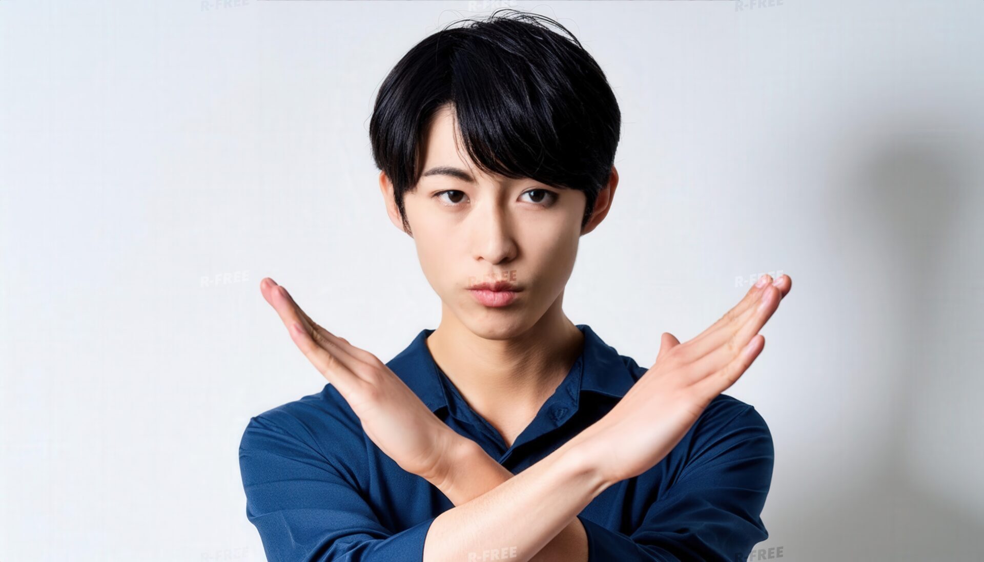 白背景でネイビーのトップスを着て腕をクロスする短髪の真剣な人