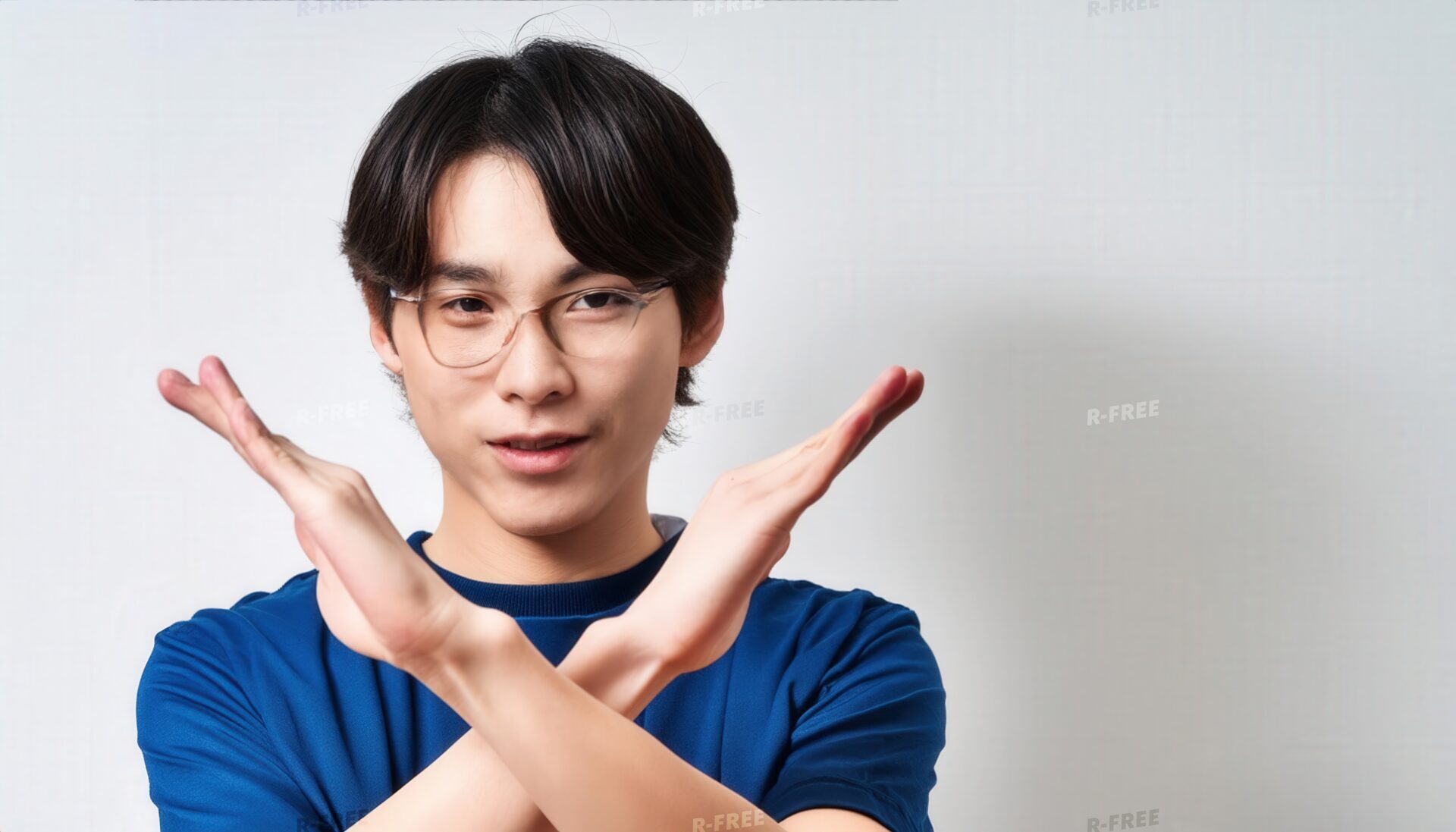 白背景で青いTシャツとメガネをかけて腕をクロスしてNGサインを示す人
