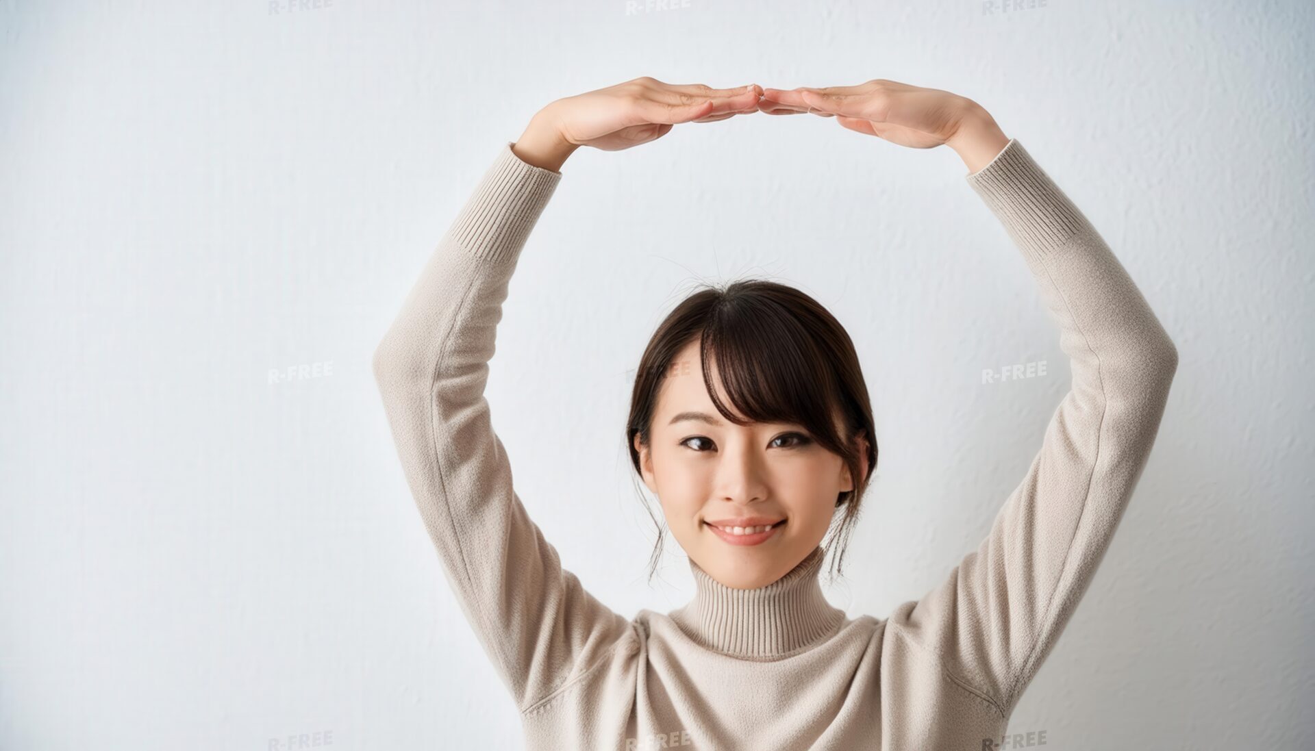 白い壁を背景に笑顔で頭上に円を作る20代女性