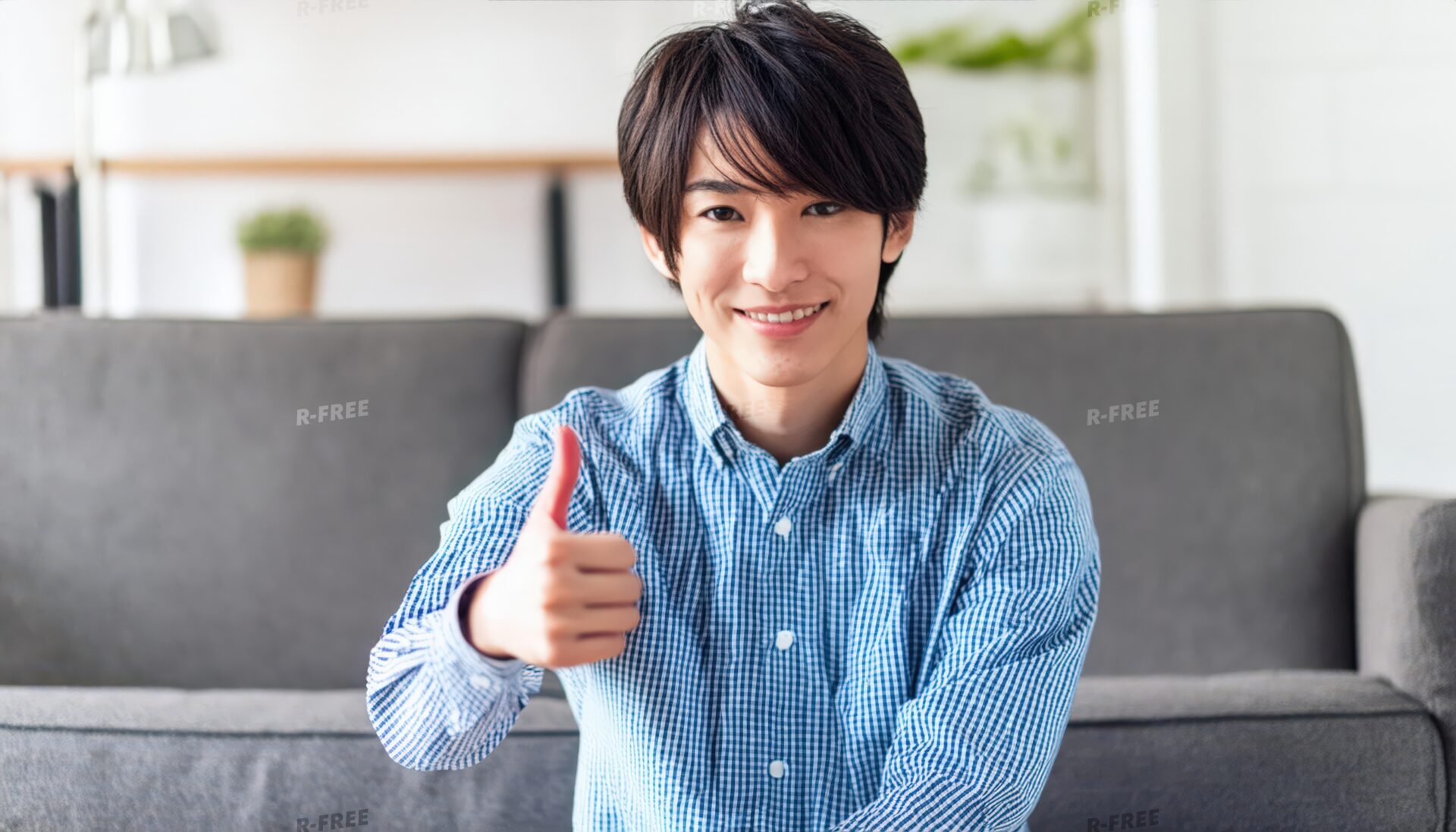 リビングで笑顔で親指を立てる青いチェックシャツの20代男性