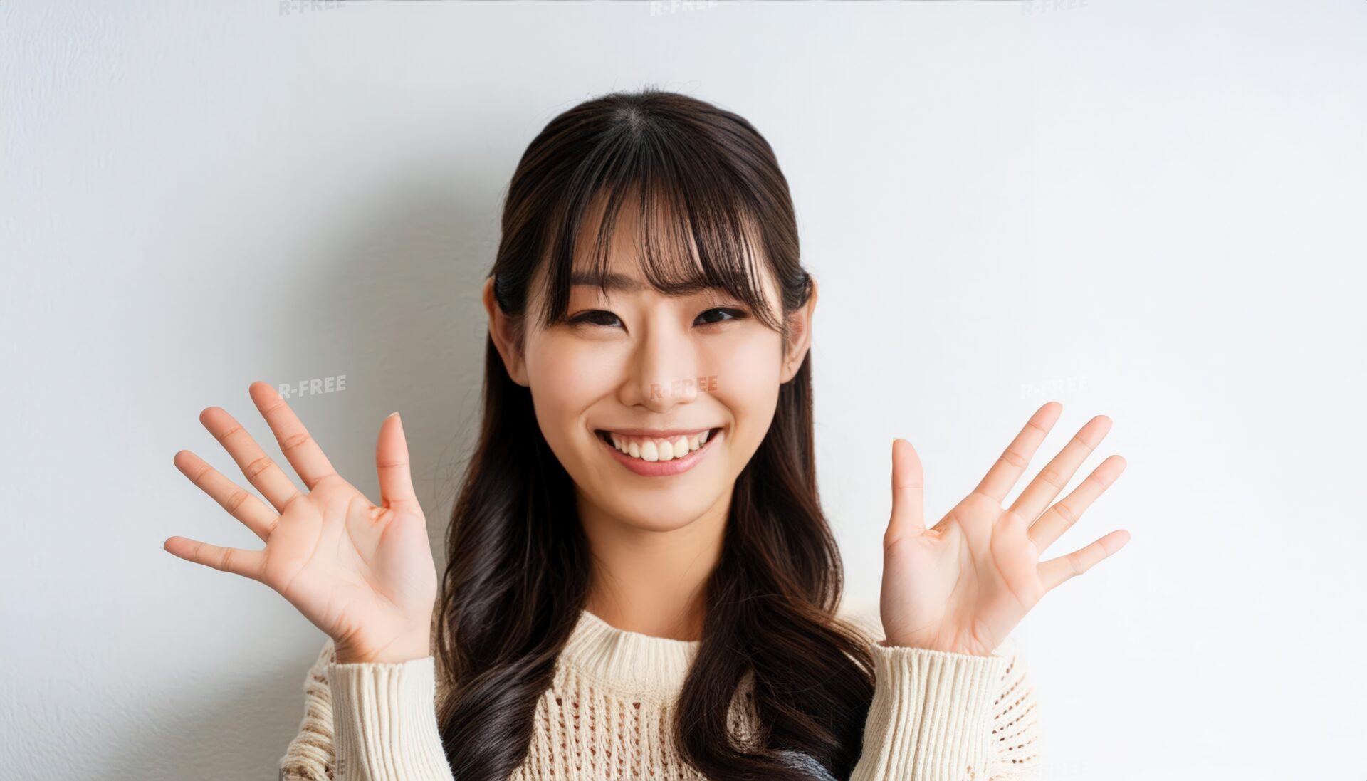 白背景で両手を広げるベージュニットを着た若い女性