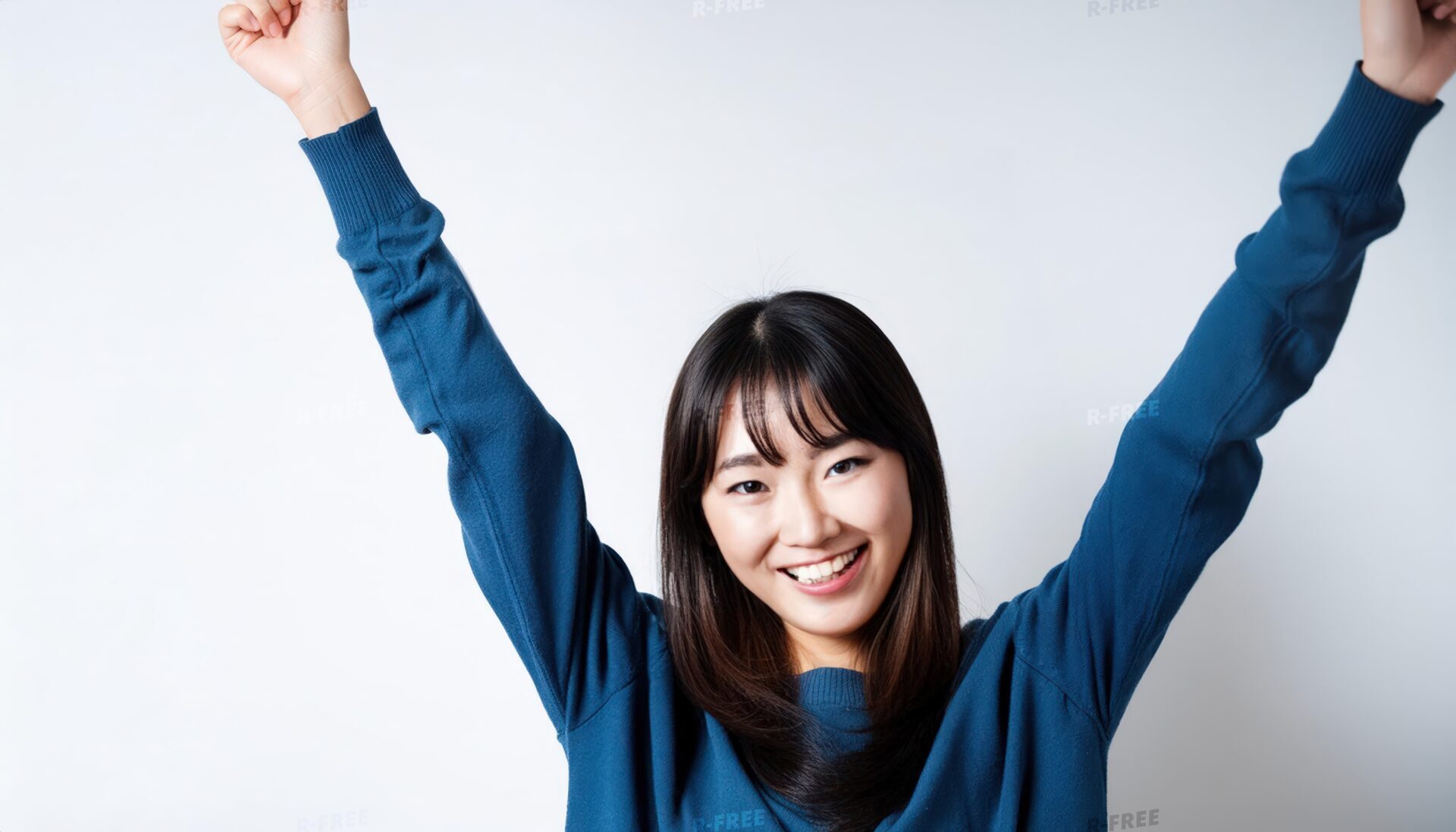 白背景で両腕を上げるブルートップスの若い日本人女性