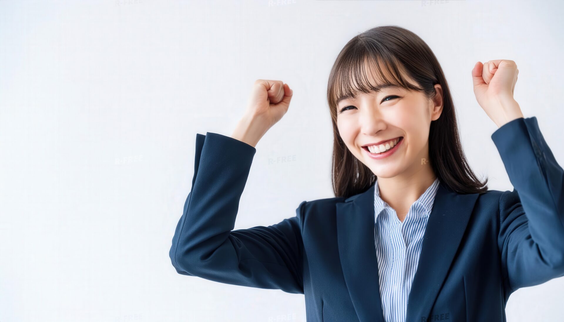 白背景でガッツポーズをする笑顔の若い女性（スーツ姿）