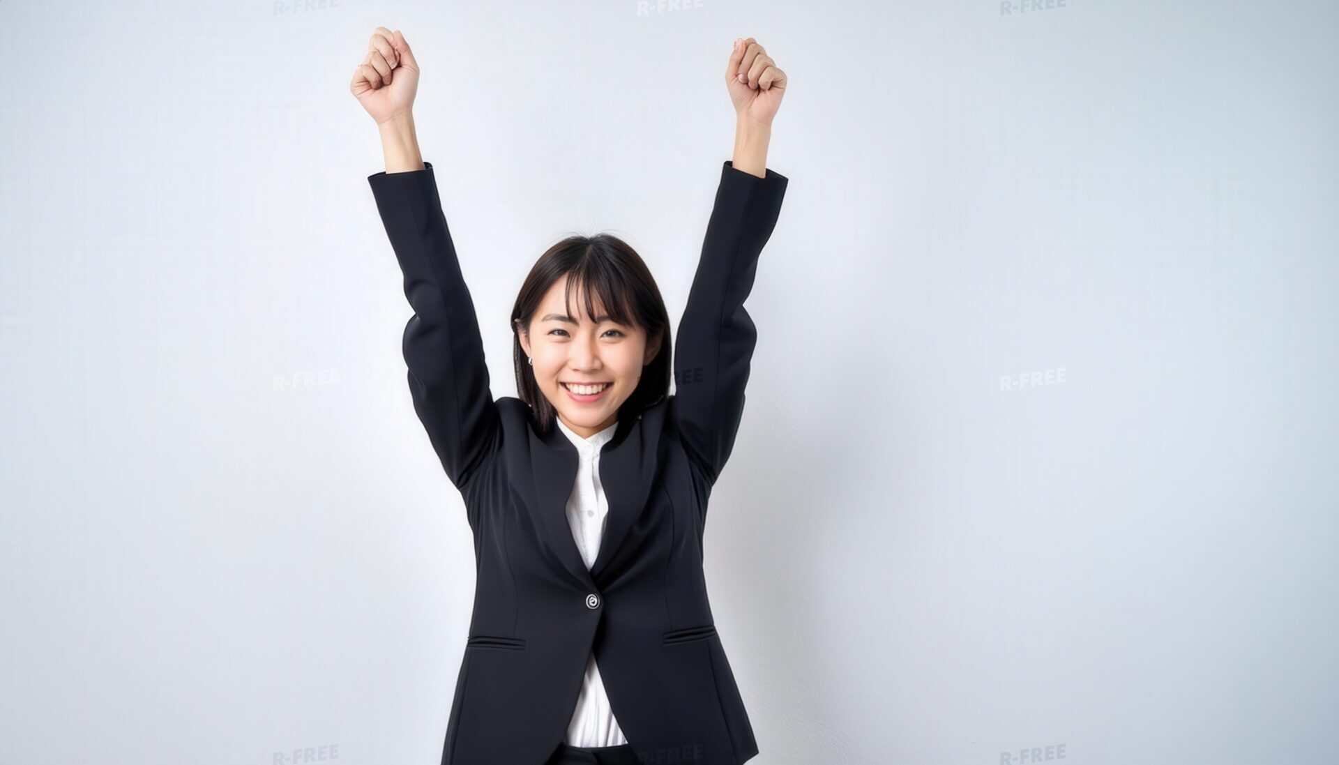 白背景で腕を上げる笑顔の若い女性（ブラックスーツ）