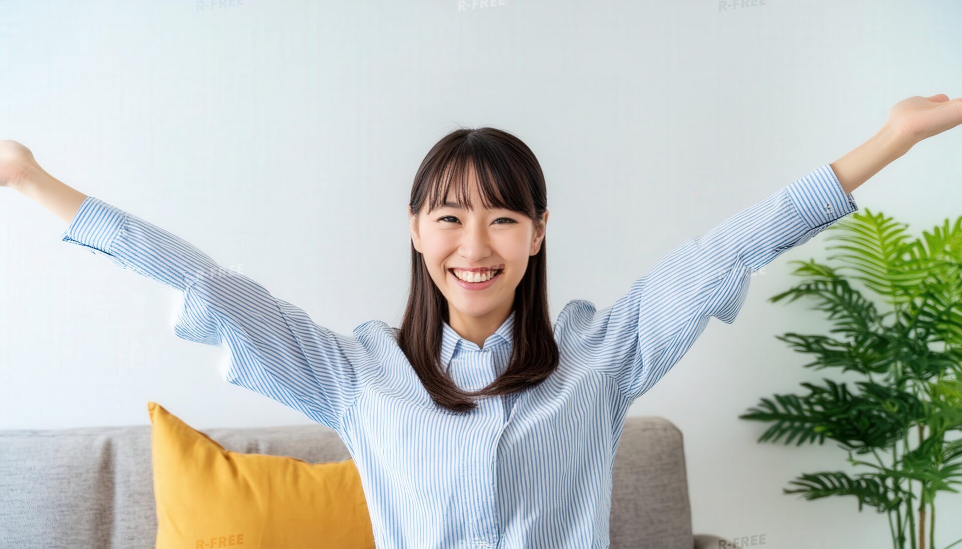 室内で両腕を大きく広げ笑顔を見せる若い女性（ストライプシャツ）