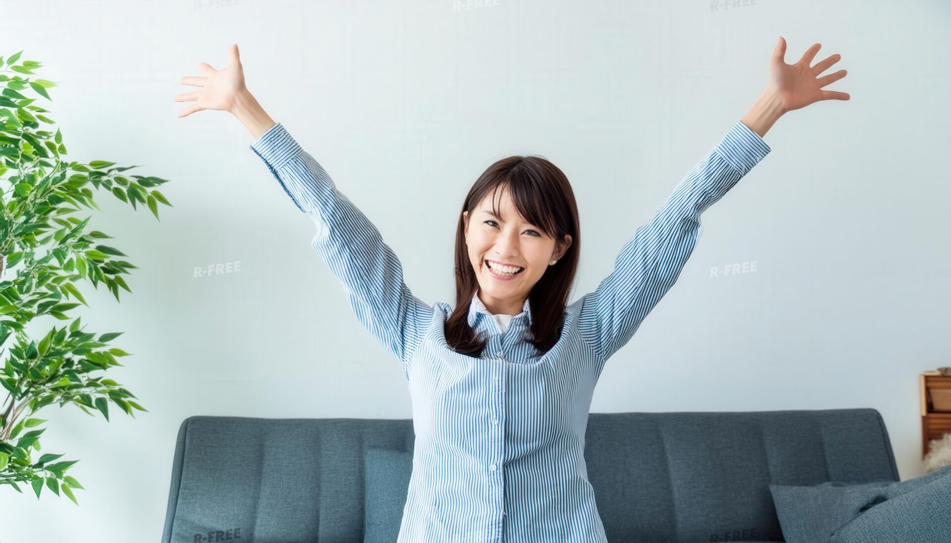 ソファ前で両腕を広げ笑顔の若い女性（ストライプシャツ）