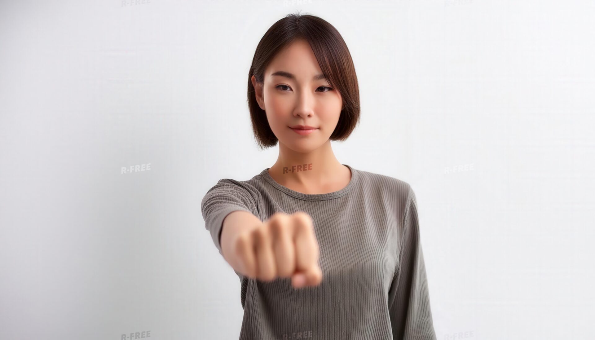 白背景で拳を突き出すグレー長袖の若い女性