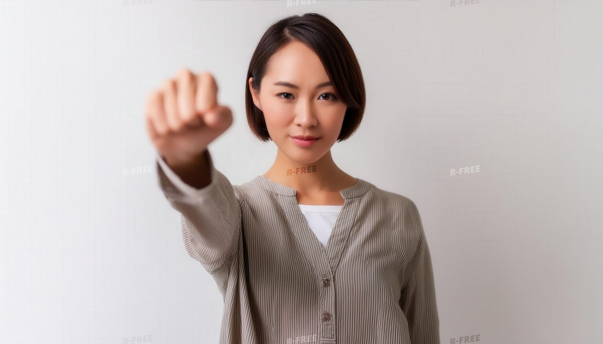 白背景で右手の拳を突き出すカーディガンの若い女性