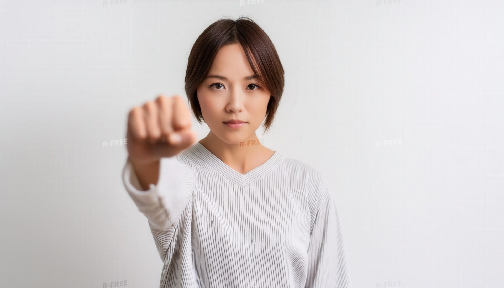 淡いグレー背景で拳をカメラに向ける若い女性
