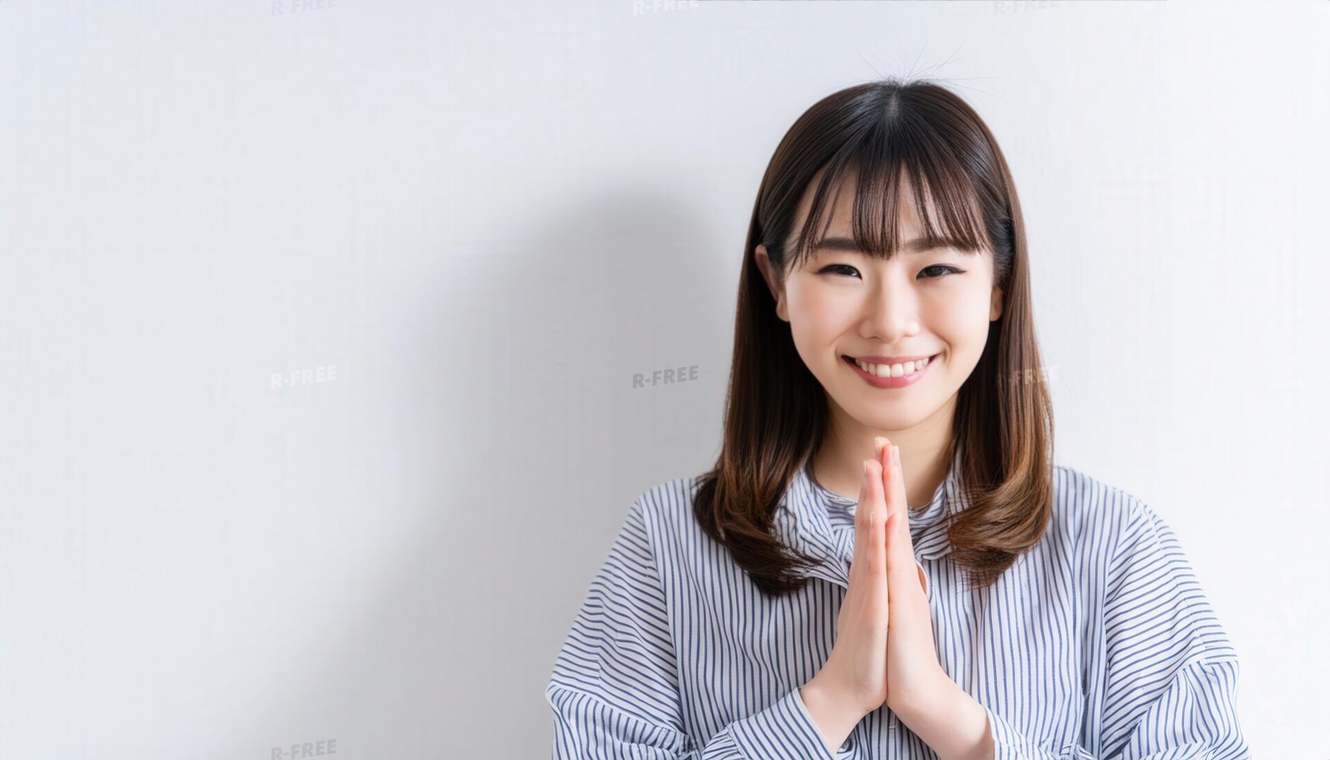 白背景で祈りのポーズをとる若い女性（ストライプシャツ）