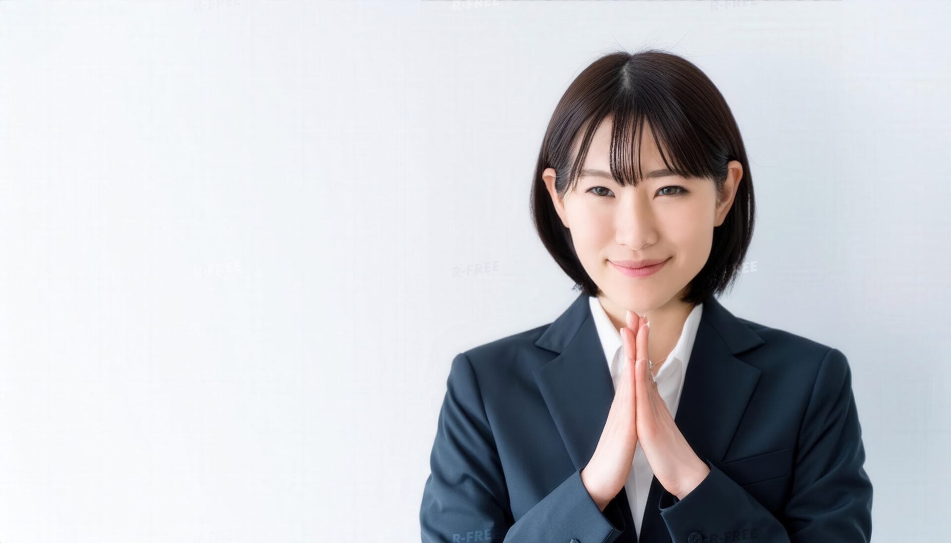 白背景で合掌するボブヘアの若い女性（紺色スーツ）