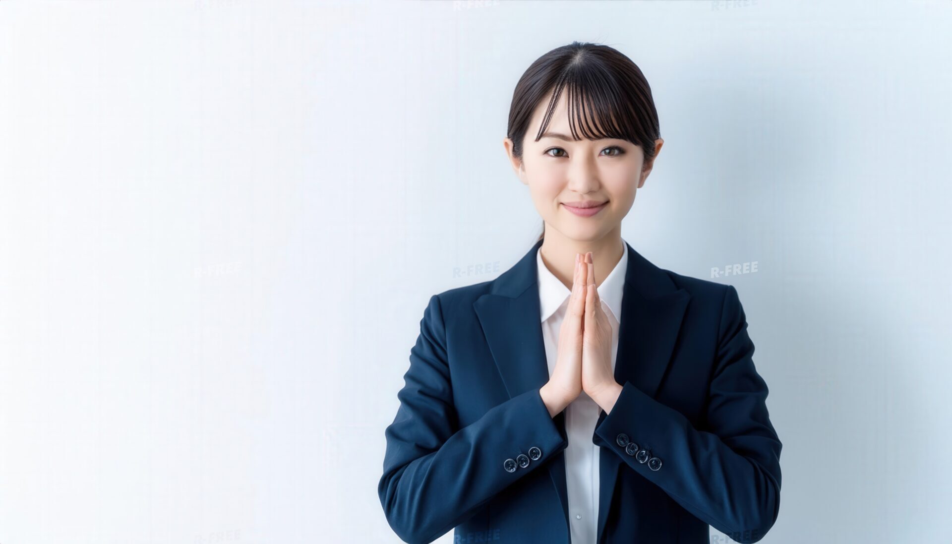 淡い青みの背景で両手を合わせ微笑む20代女性の上半身