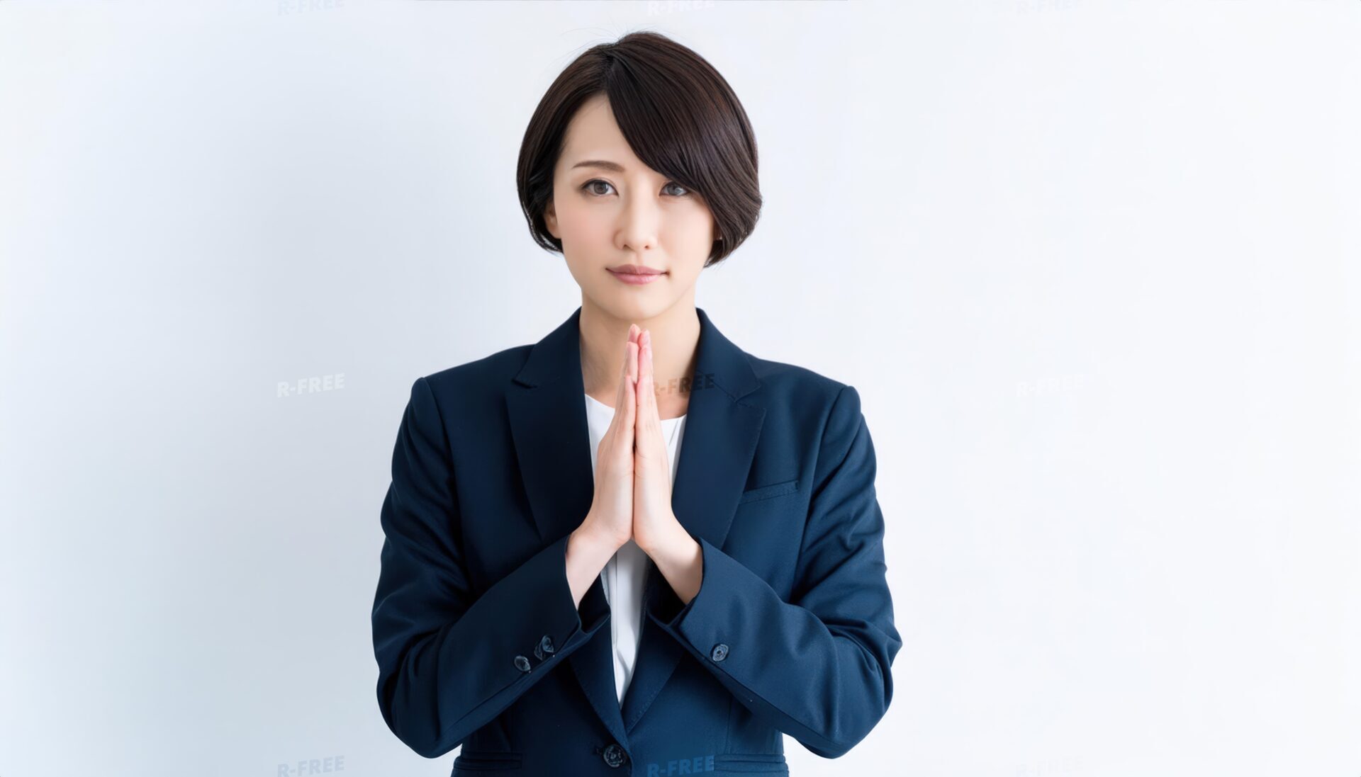 白背景で祈りのポーズをする若い女性（スーツ）