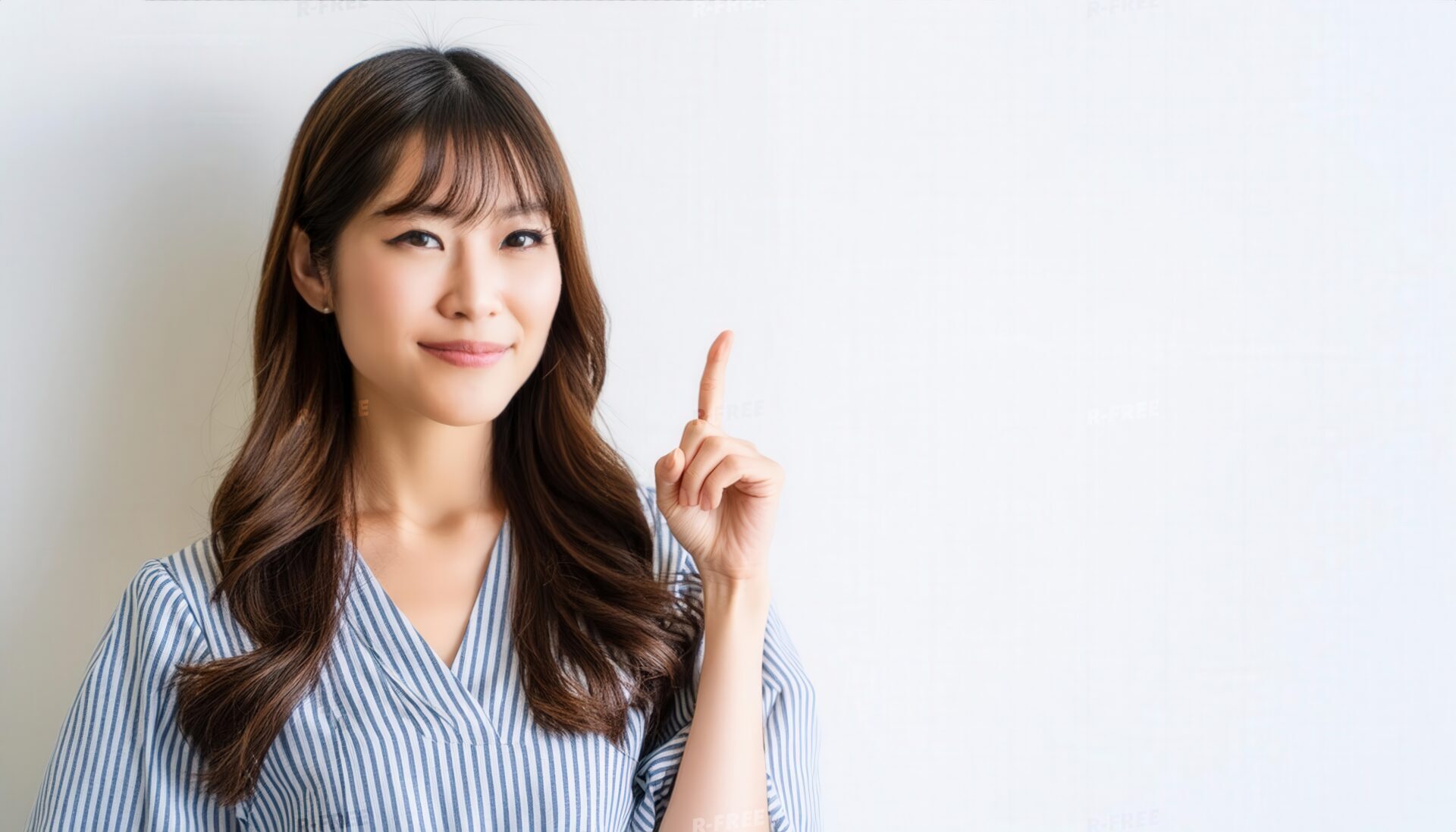 白背景で人差し指を立てる若い女性（ストライプトップス）
