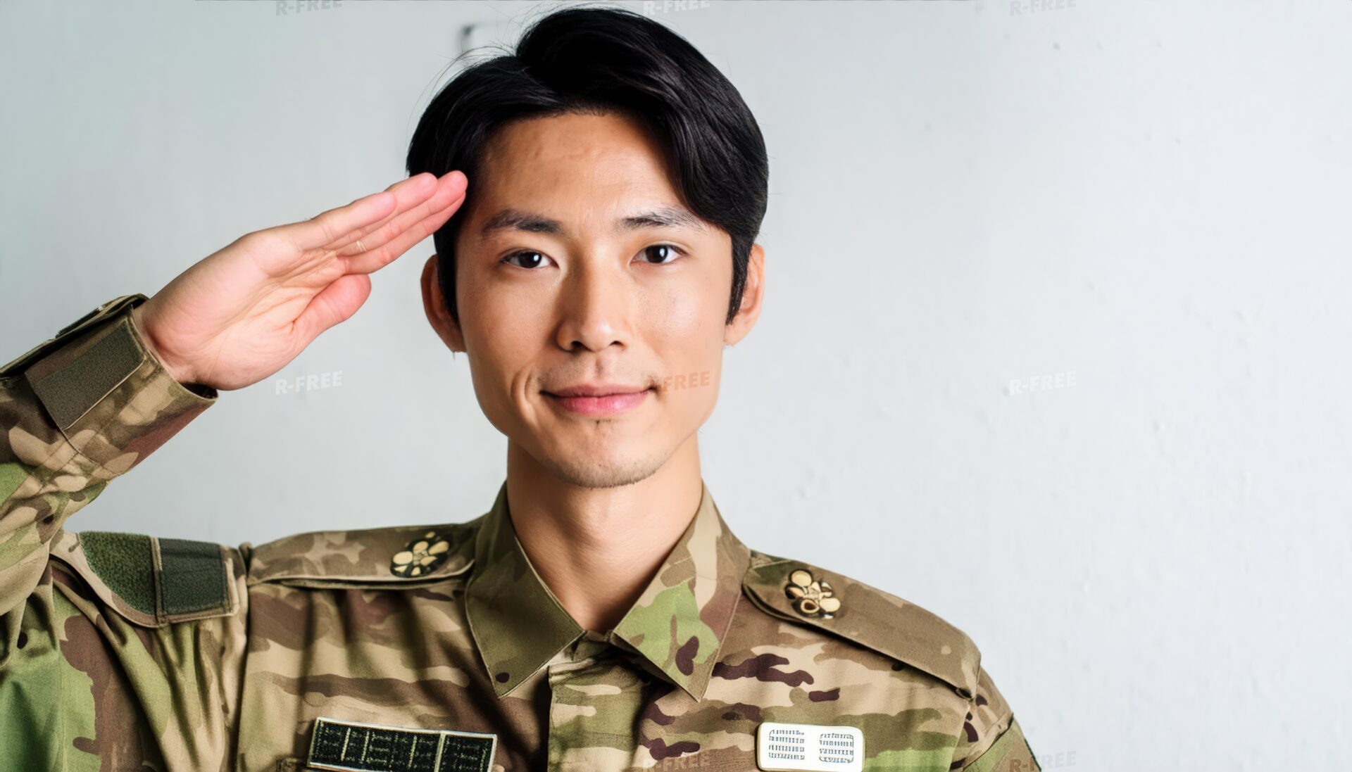 室内で正面を向き敬礼する迷彩服の軍人
