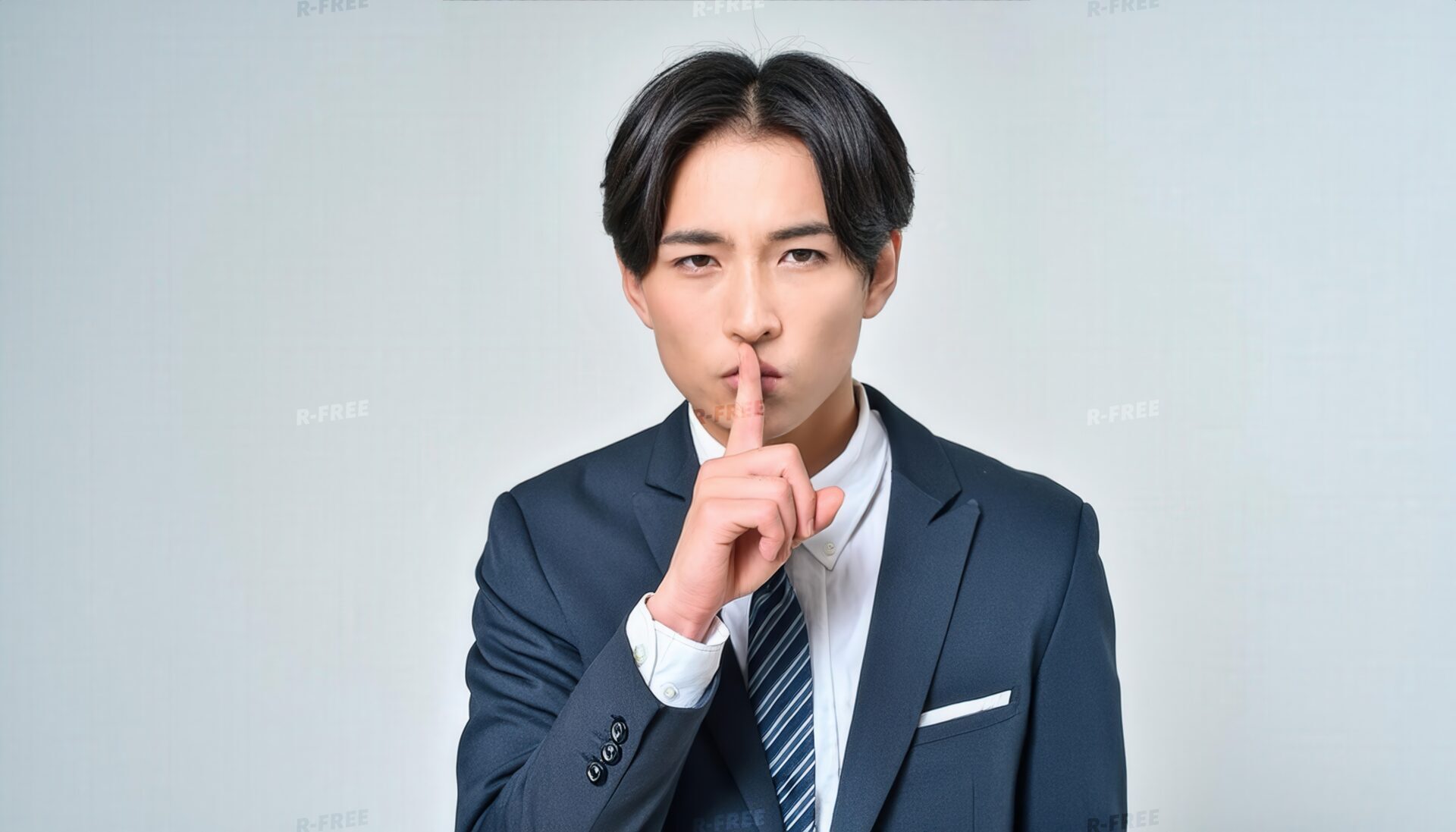 口元に指を当て黙る黒髪センター分けの20代男性