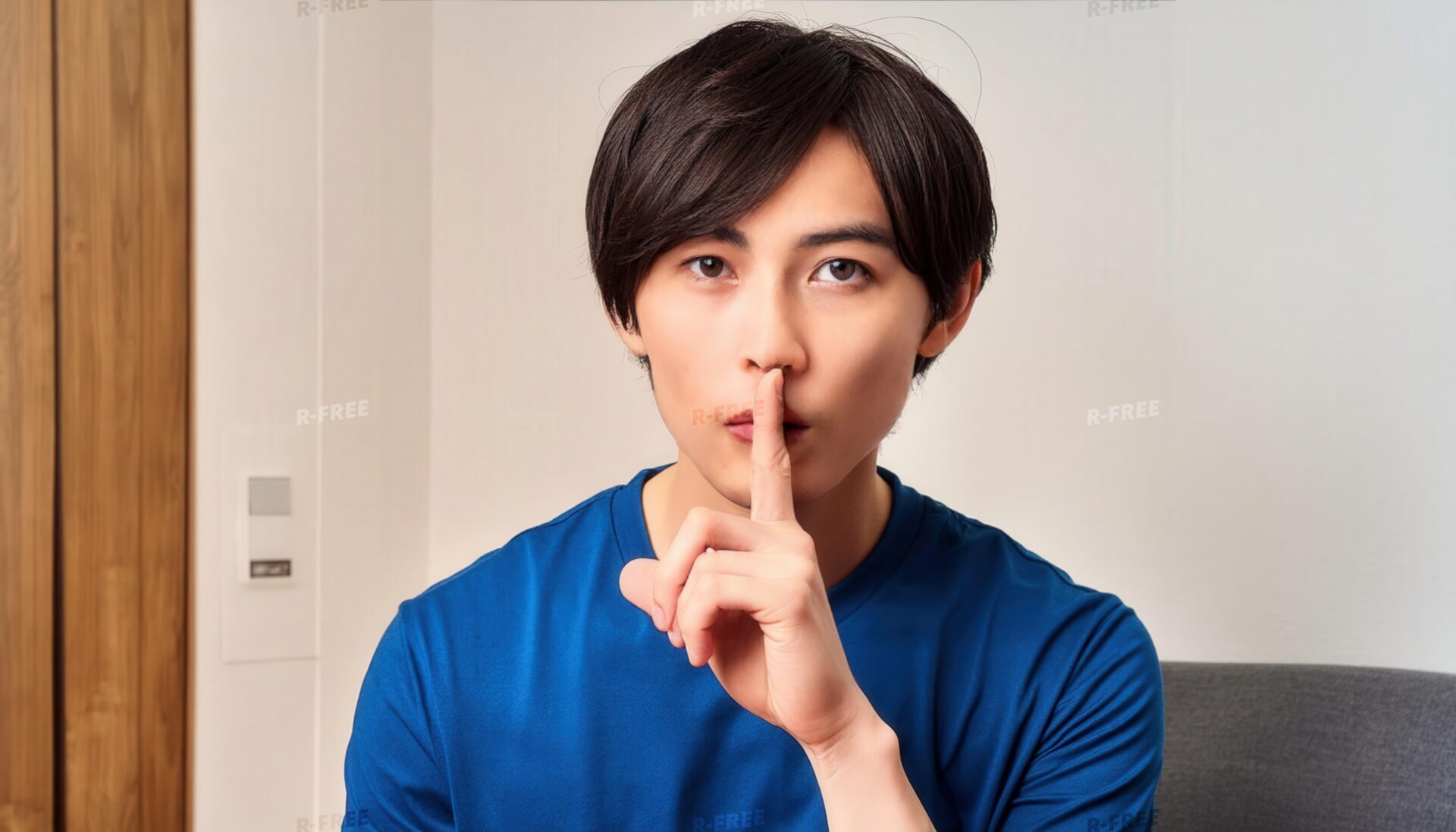室内で口元に指を当て静かにするポーズをとる若者