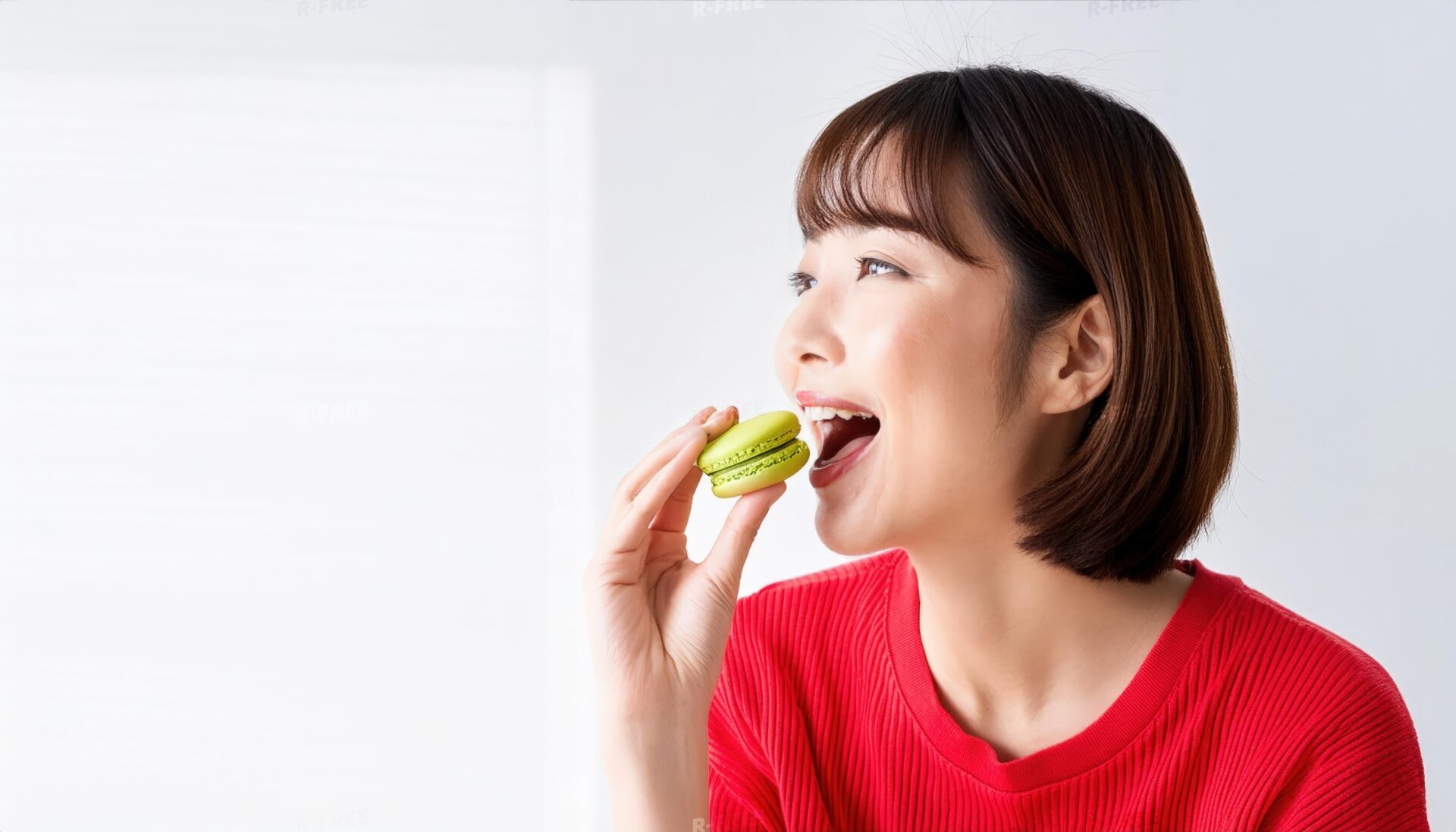 笑顔で緑色のマカロンを食べようとする赤いトップスの女性
