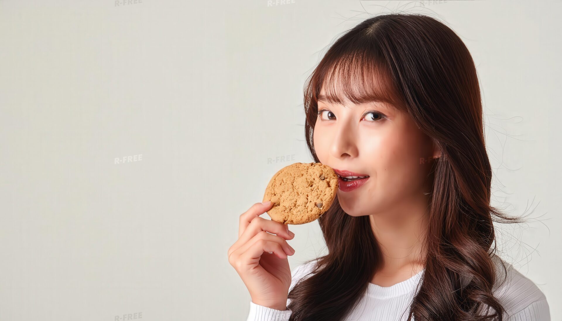 白い服でクッキーを口元に運ぶロングヘアの女性
