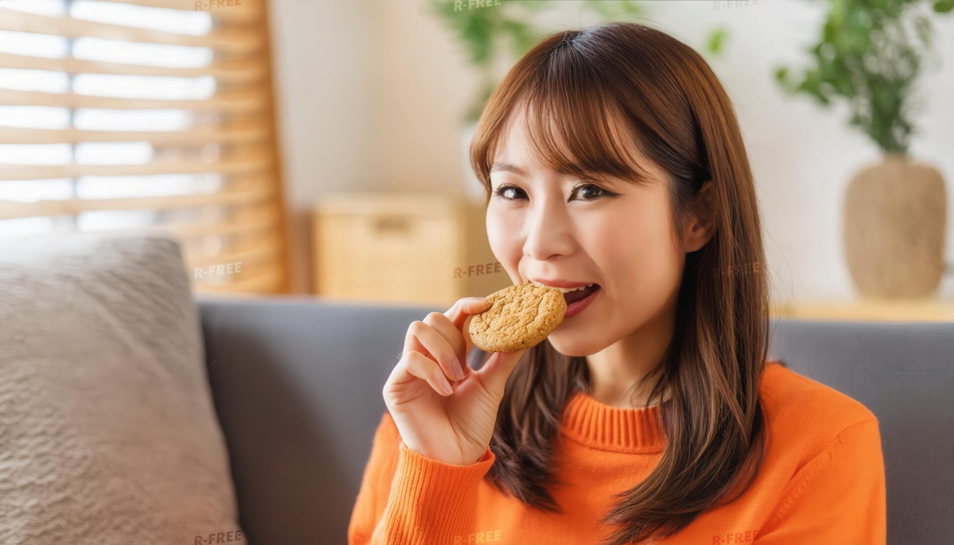 オレンジ色のニットでクッキーを食べる女性