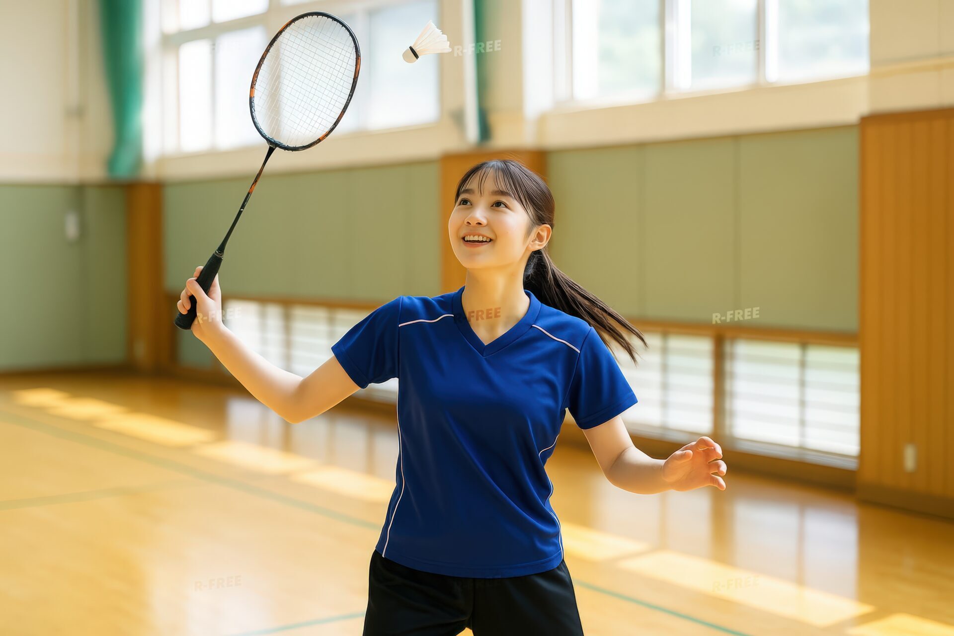 バドミントンのシャトルを打つ笑顔の女子学生