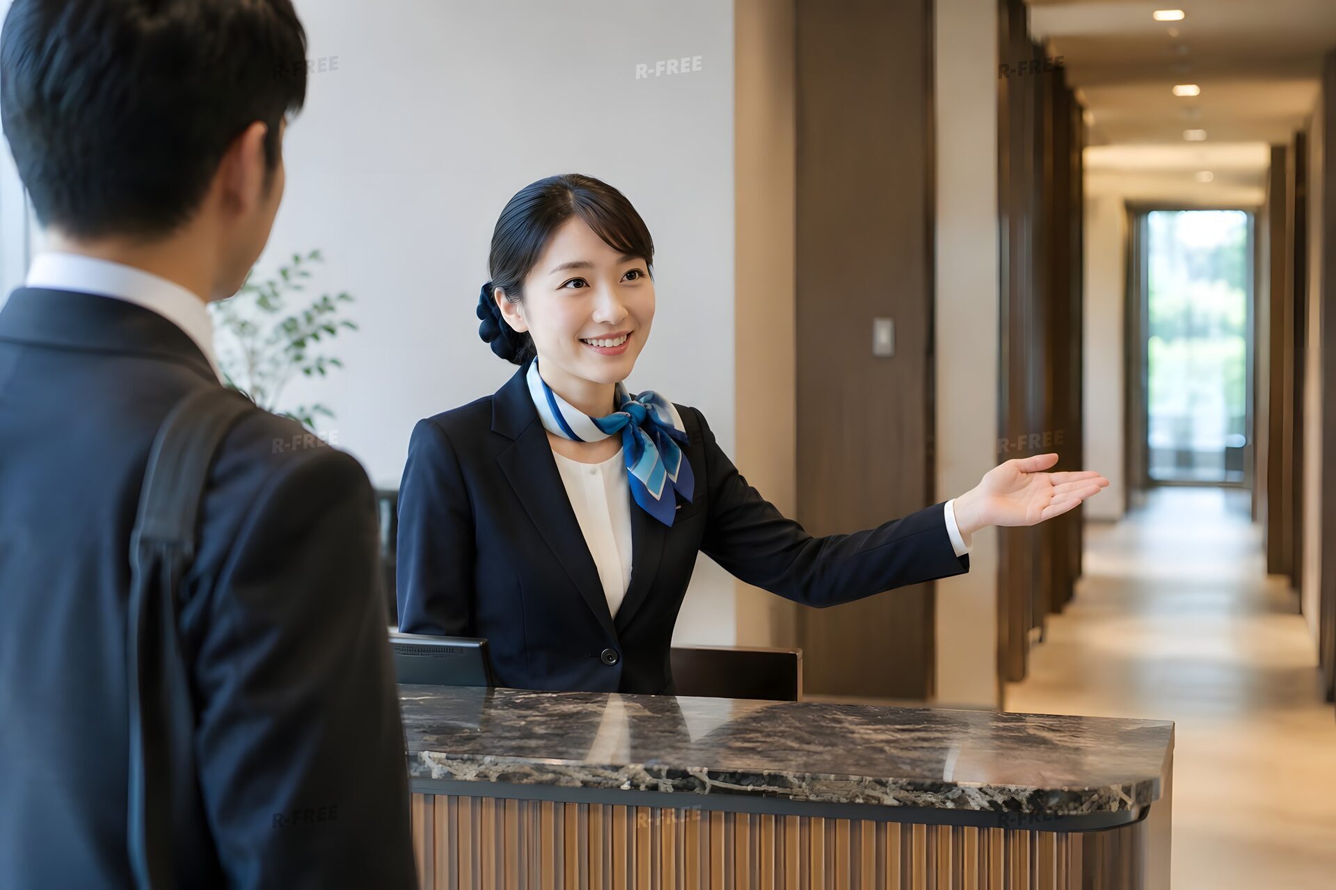 受付で来客を手で案内する20代の受付女性