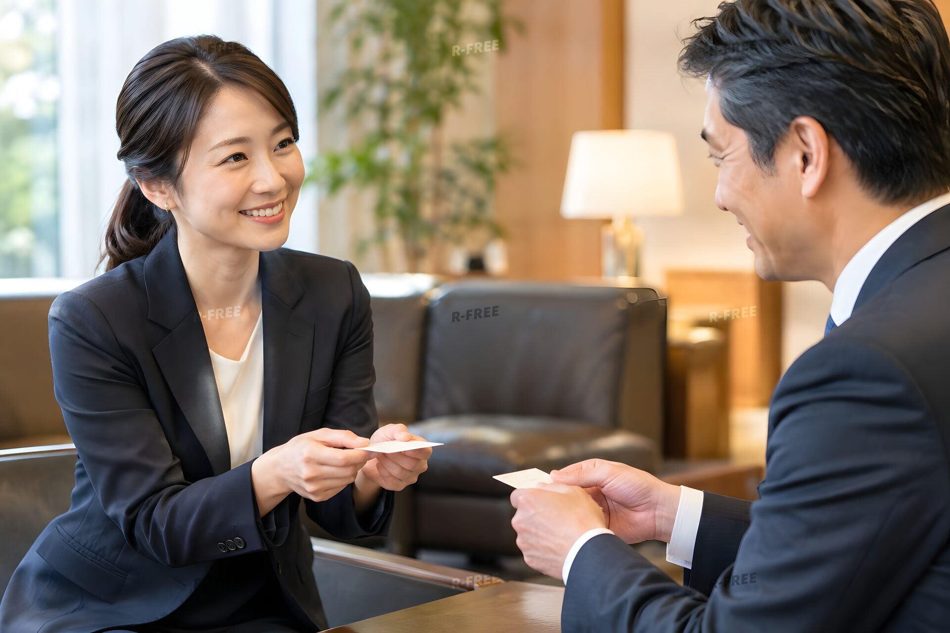 応接室で取引先と笑顔で名刺交換をする30代女性