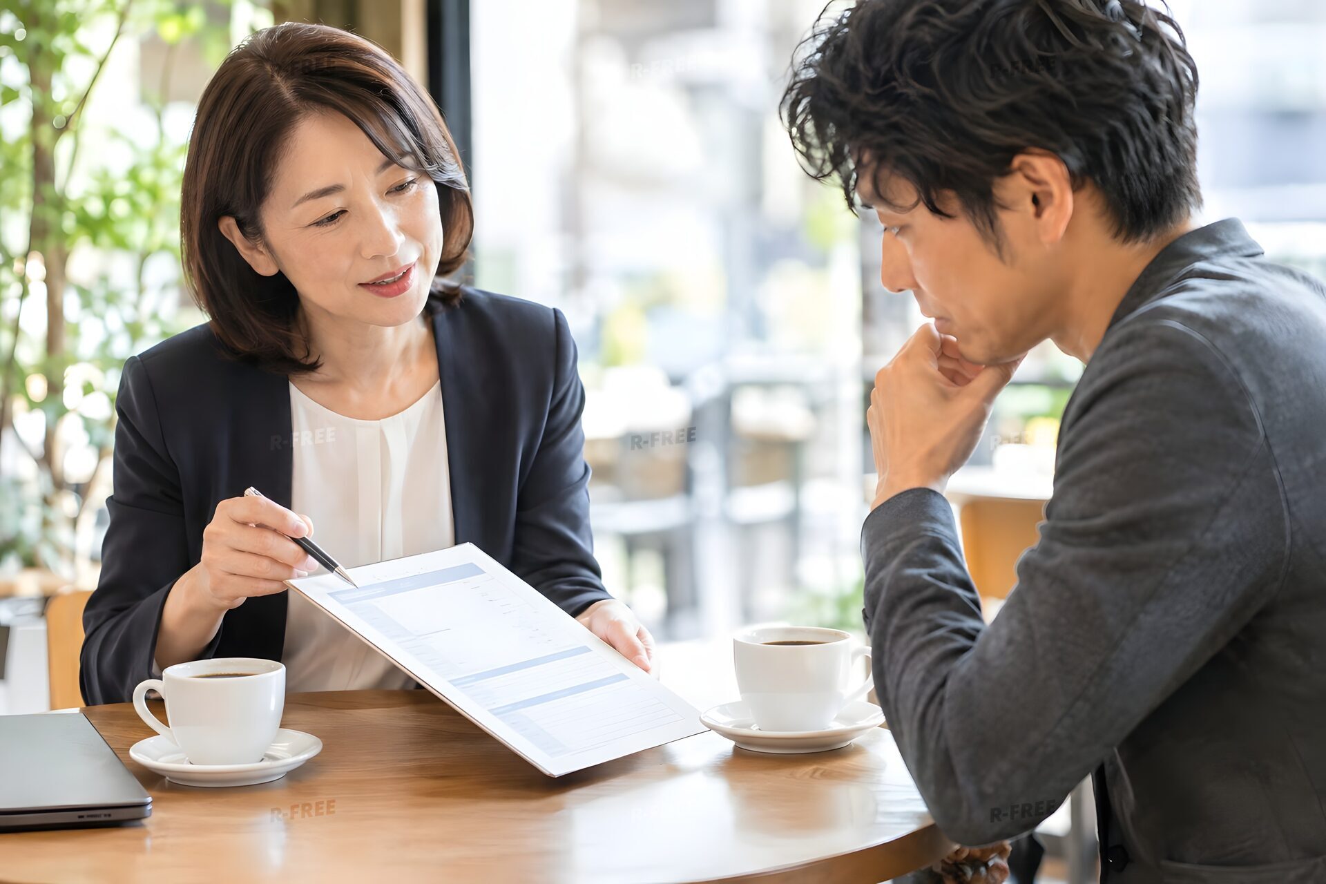 カフェのテーブルで見積書を示す40代女性と検討する取引先