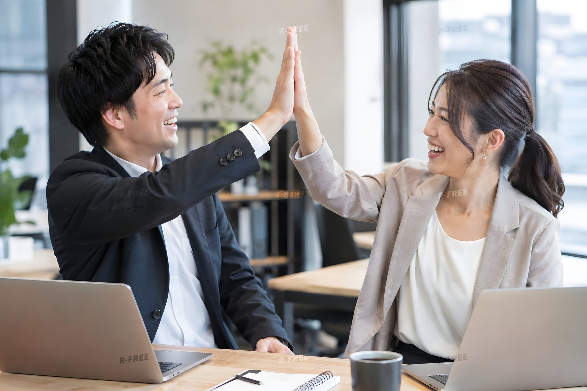 プロジェクト完了を祝ってデスク越しにハイタッチする同僚