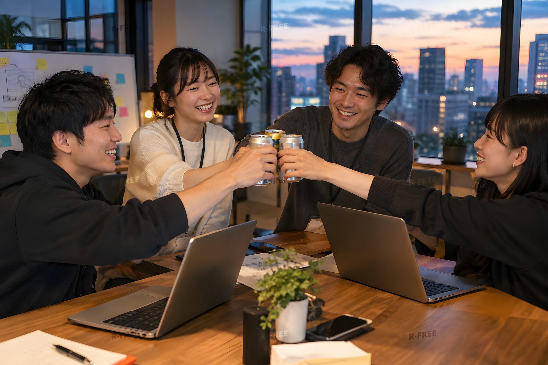 夕暮れのオフィスで缶飲料で乾杯する4人のスタートアップチーム