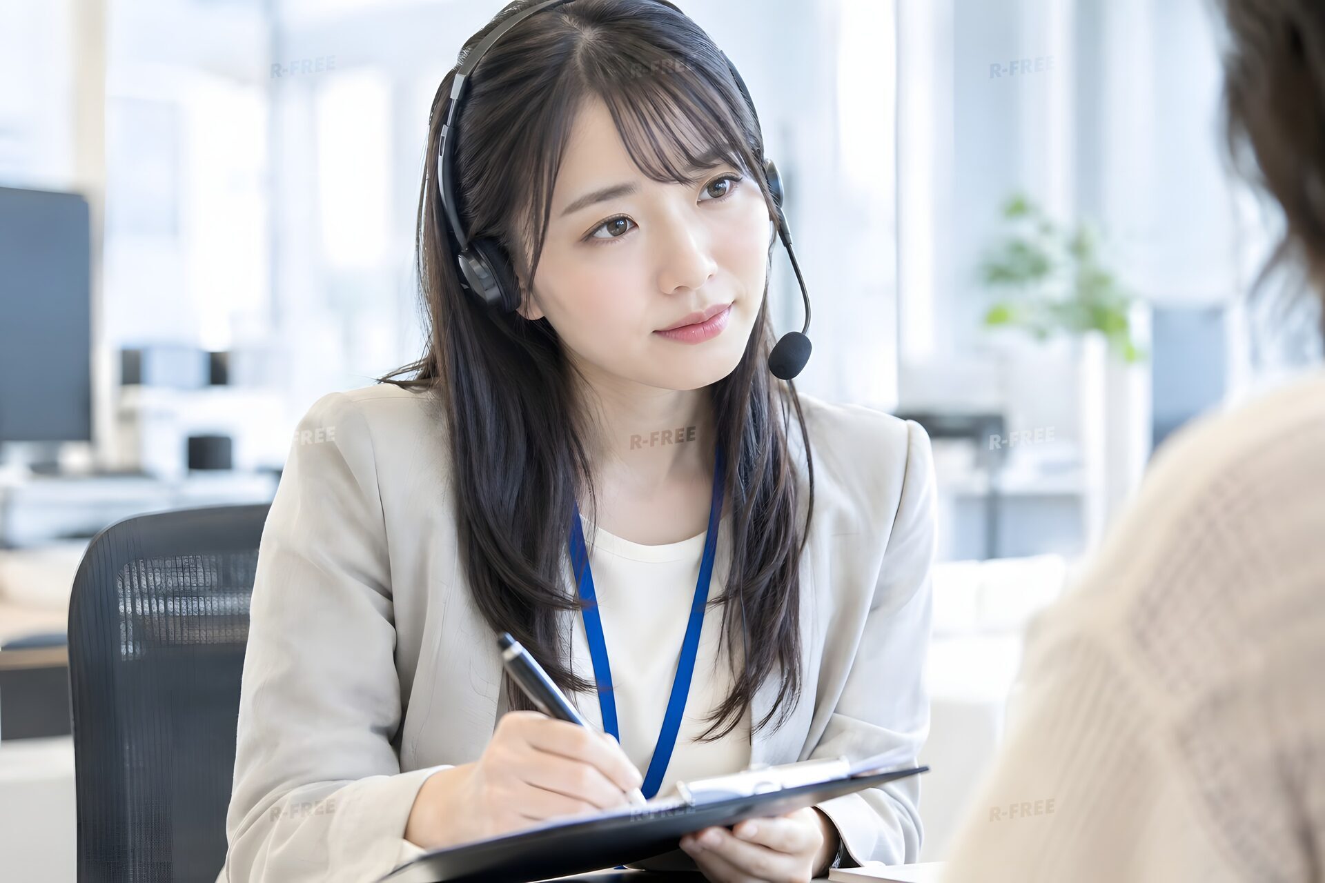 苦情の内容を用紙に書き留めるヘッドセットの20代女性